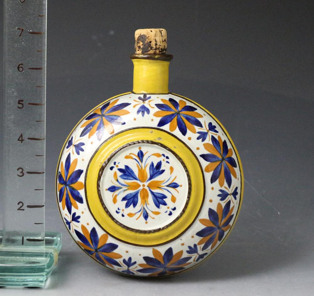 Prattware pottery spirit flask decorated with dark ochre and blue flowers, 1815 Staffordshire England. 

A fine example of a prattware pottery spirit flask decorated with dark ochre and blue flowers and embellished with yellow-banded circles. The
