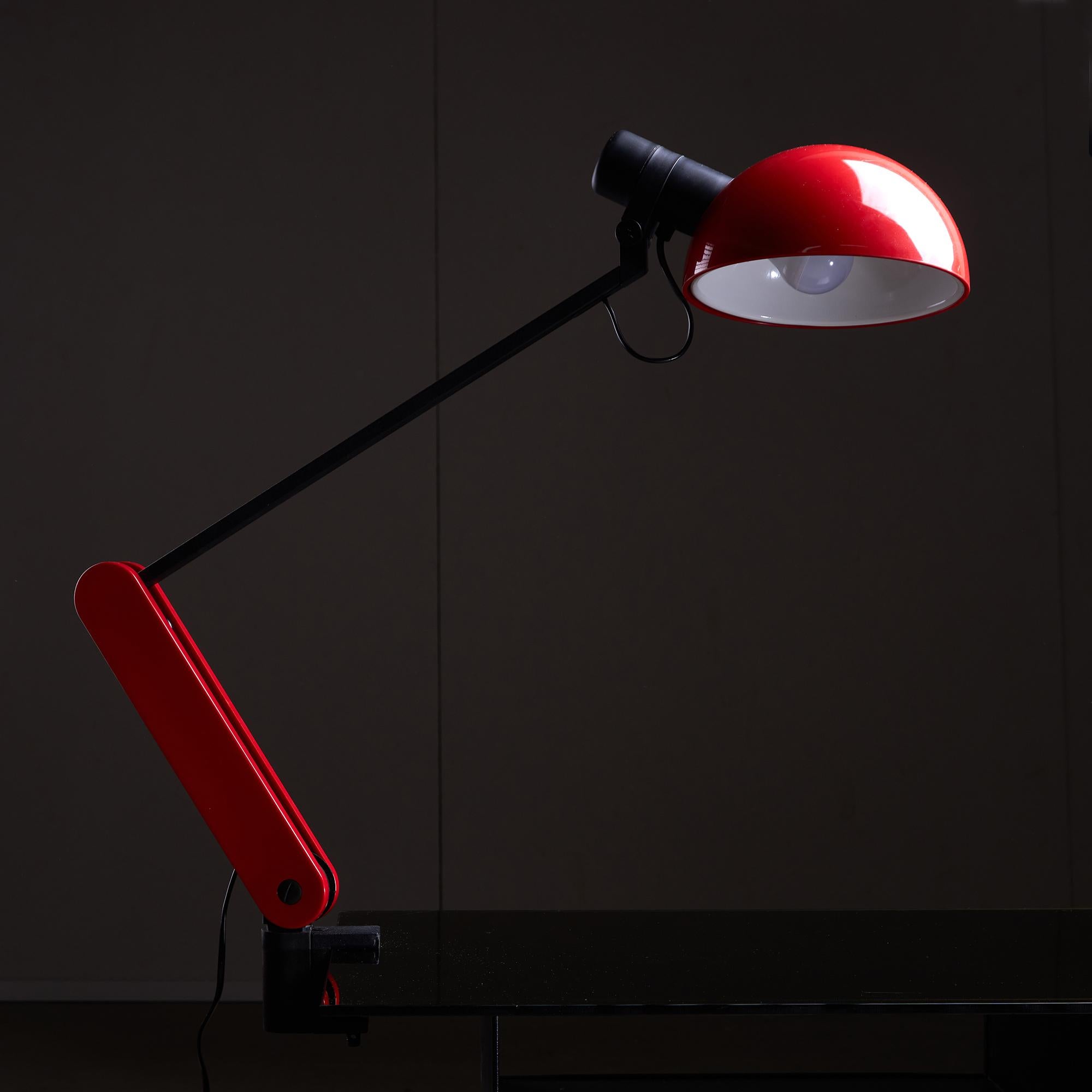 The Praxi Table Lamp, designed by Bruno Umberto Gecchelin for Guzzini in 1982, blends functionality with modern aesthetics. Its sturdy black metal body is complemented by a bright red sponge-shaped plastic accent, creating a lively focal point. The