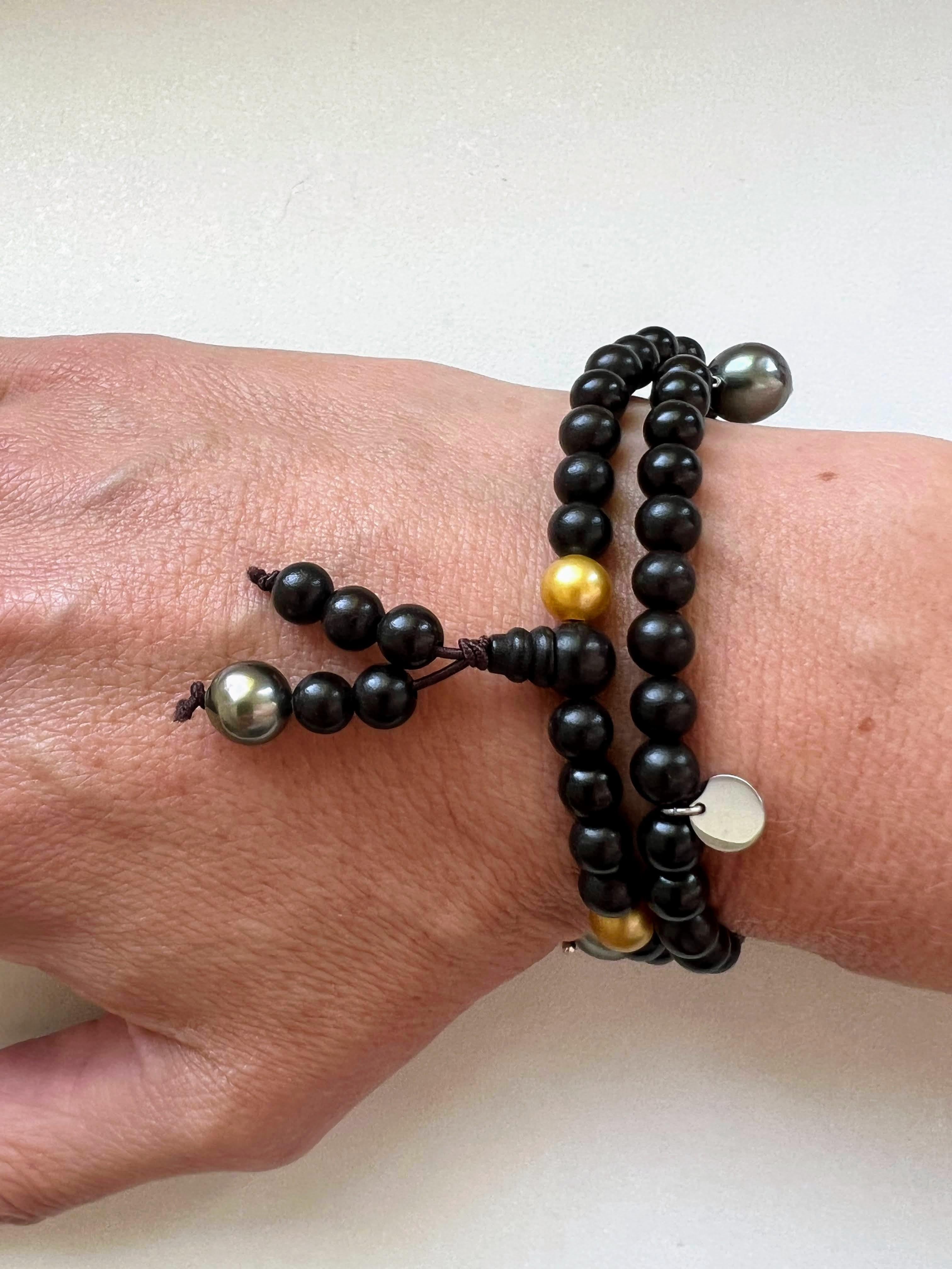 Ce bijou s'inspire des bracelets de prière bouddhistes. Il peut être porté comme un collier court ou enroulé autour du poignet. Il est captivant avec ses petites perles dorées intrigantes et rares. Les perles de Tahiti pendantes de forme baroque