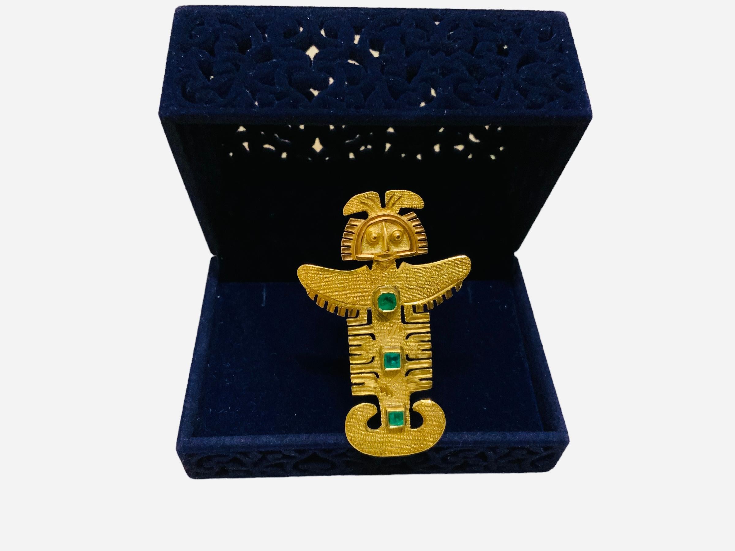 This is an 18K Yellow gold and Emerald hand crafted Pre-Columbian large brooch/pendant. It depicts a Central America Native God adorned in the center with a column of three square emeralds that measure 3mm each one. Its weight is 8.7 dwt. It is