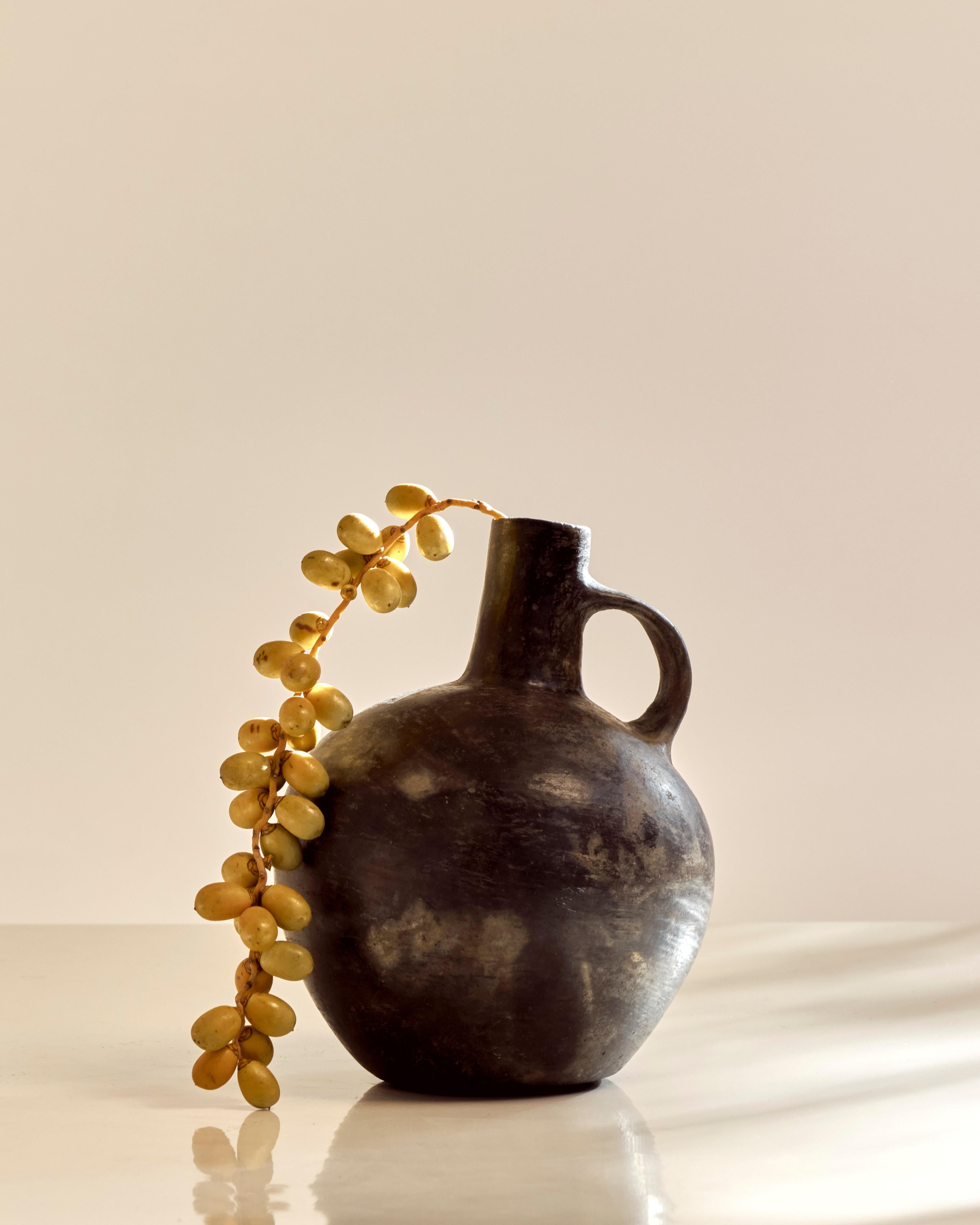 Pre-Columbian Blackware Vessel from the Chimu/Inca Culture with looped handle and narrow bottleneck. Peru circa 1100 to 1532. The vessel has a spherical body, a flat base, conical spout, and a ribbon-form handle.