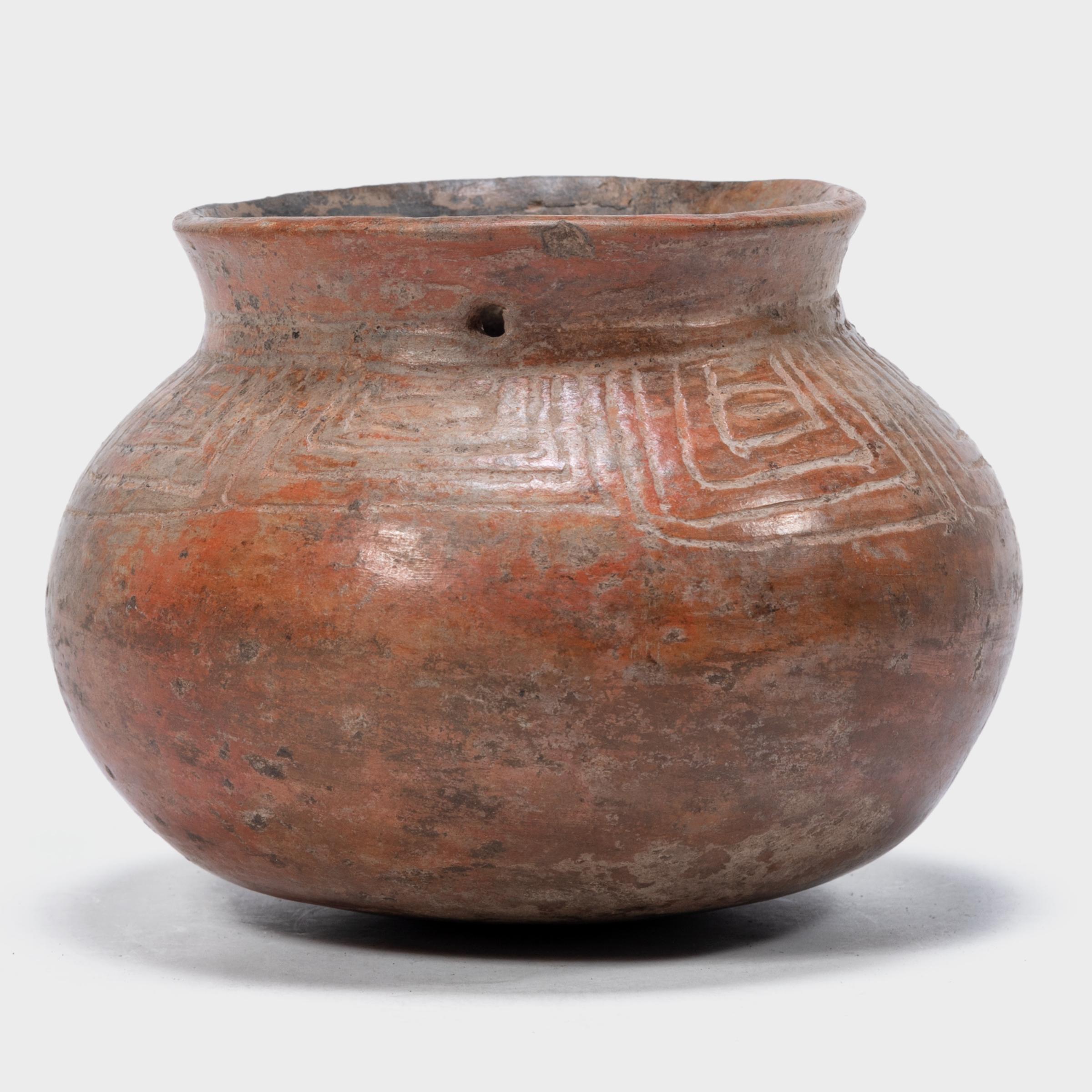 Exhibiting a rich patina, this petite redware vessel shows many telltale signs of Pre-Columbian pottery. Speckled with imperfections, the vessel's warm red-orange coloration was achieved by applying a mineral-rich slip for a monochrome finish. The