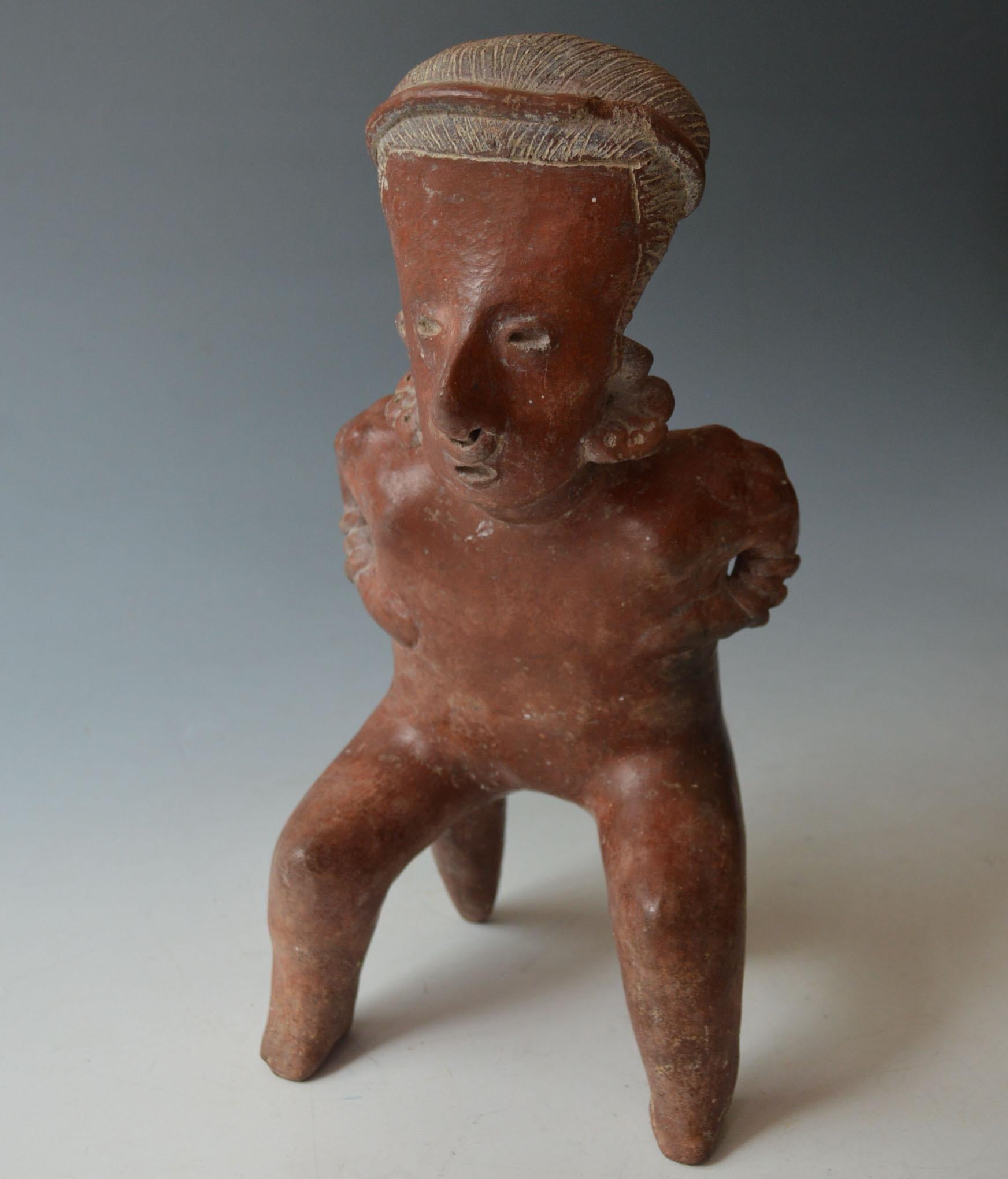 A Pre Columbian Jalisco seated figure
Jalisco West Mexico  circa B.C. 100-300 A.D,

A  Male pottery figure with red slip with elongated head and linear delineated hair wearing ear and nose ornaments,  the slim body  finely modelled with hands on