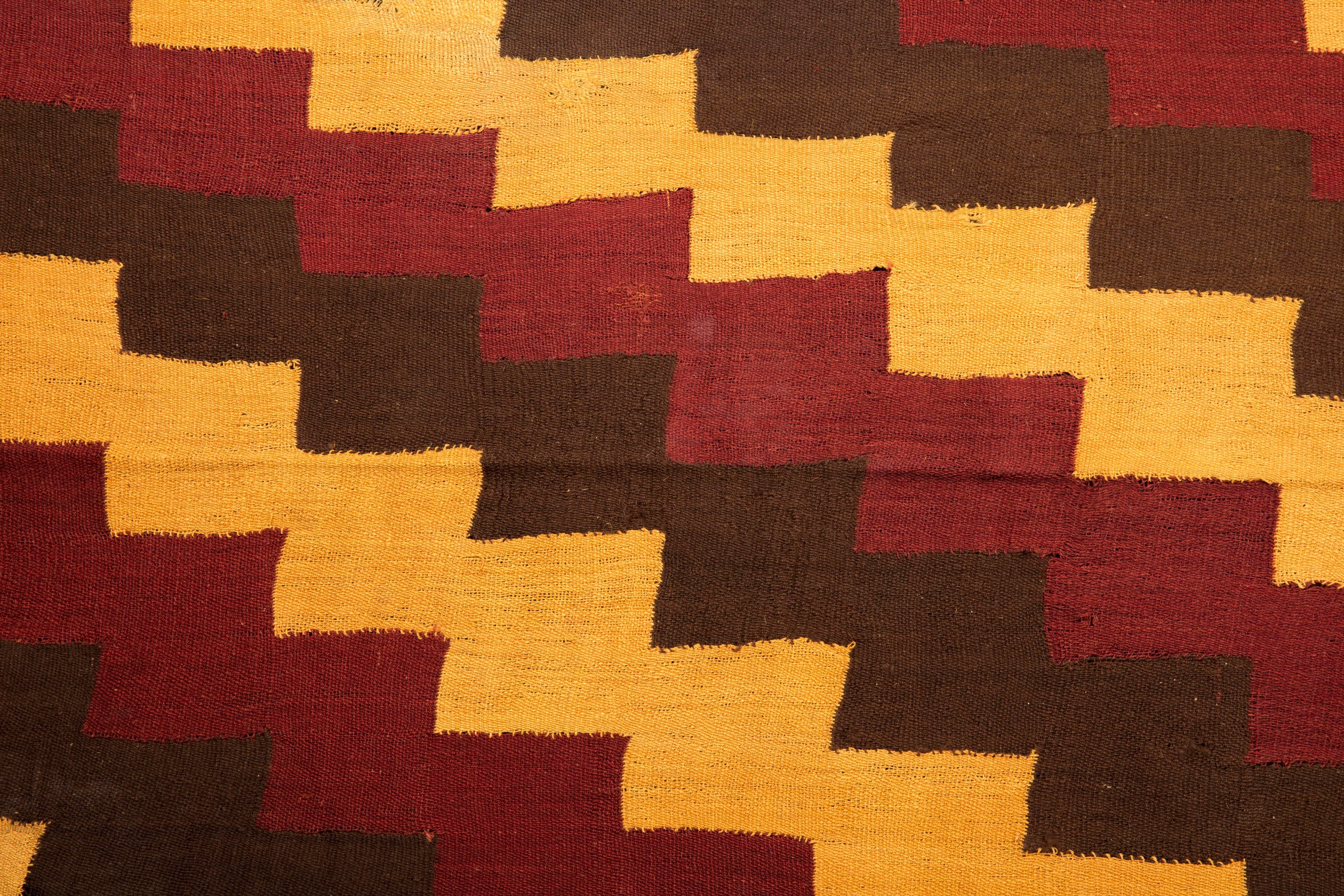 Complete Pre-Columbian Nazca textile with stepped zig-zag design in yellow, ochre red, and brown/black shades with yellow fringes.