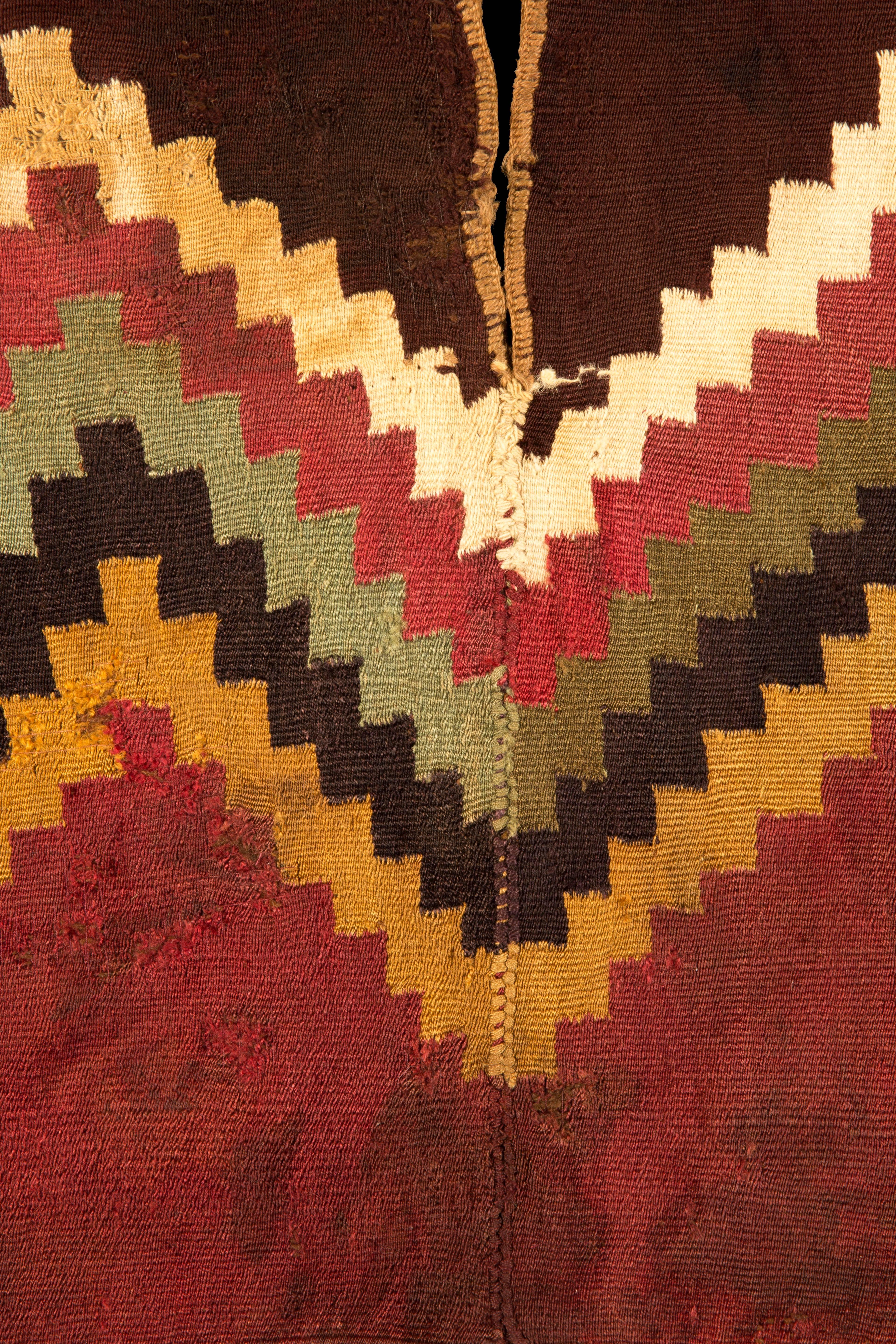 Complete Nazca unku with white, red, green, black and yellow step zig-zag design with red bottom with fringe and maroon upper part and beige trim around the arm and neck openings

200-300 CE

Nazca, Peru

Size: 38 in x 18 in.