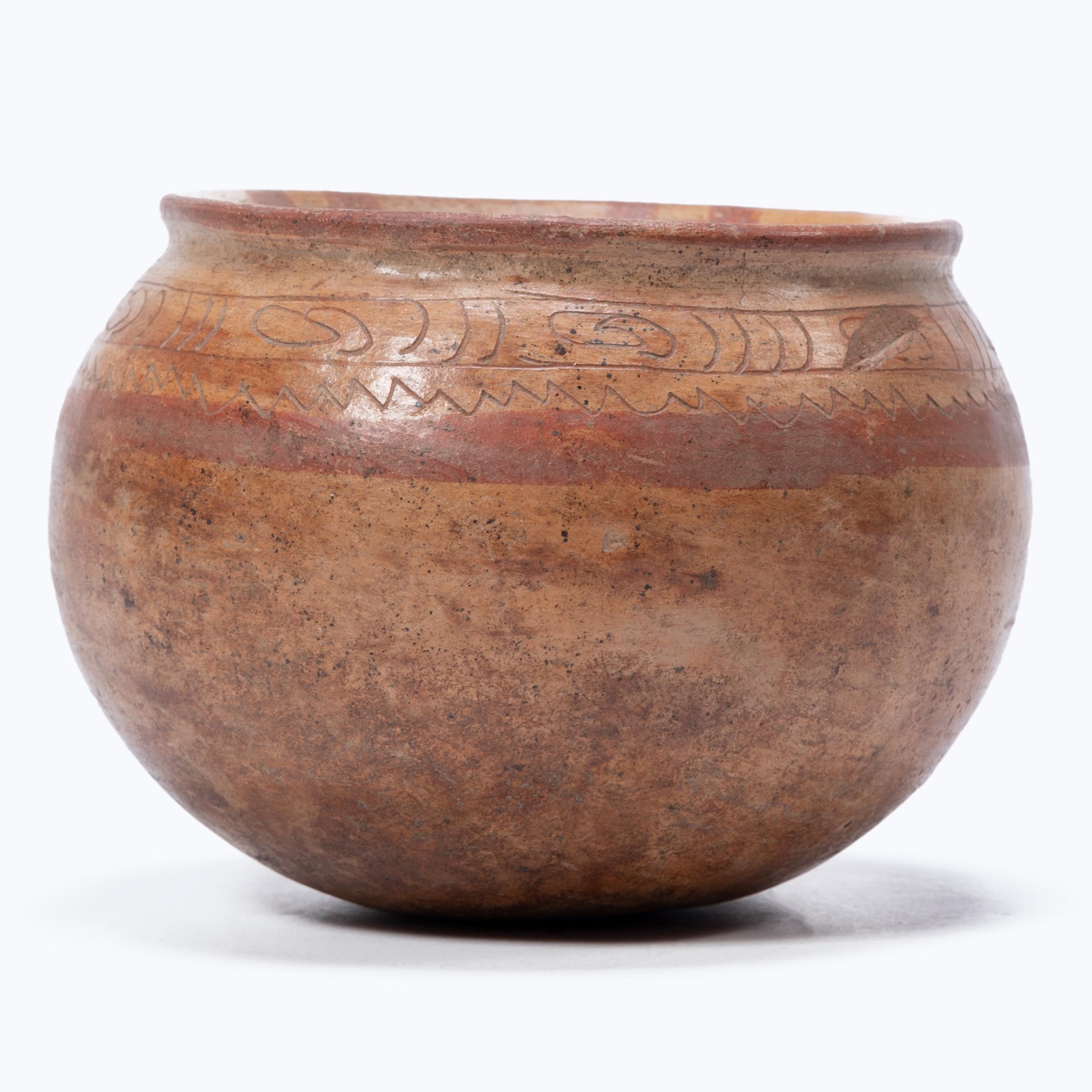 With a worn, glossy finish, this round orangeware bowl is a wonderful example of Pre-Columbian pottery. The delicate bowl has a flared lip banded by incised geometric patterns and painted red clay slip. Centuries of use have speckled the vessel with