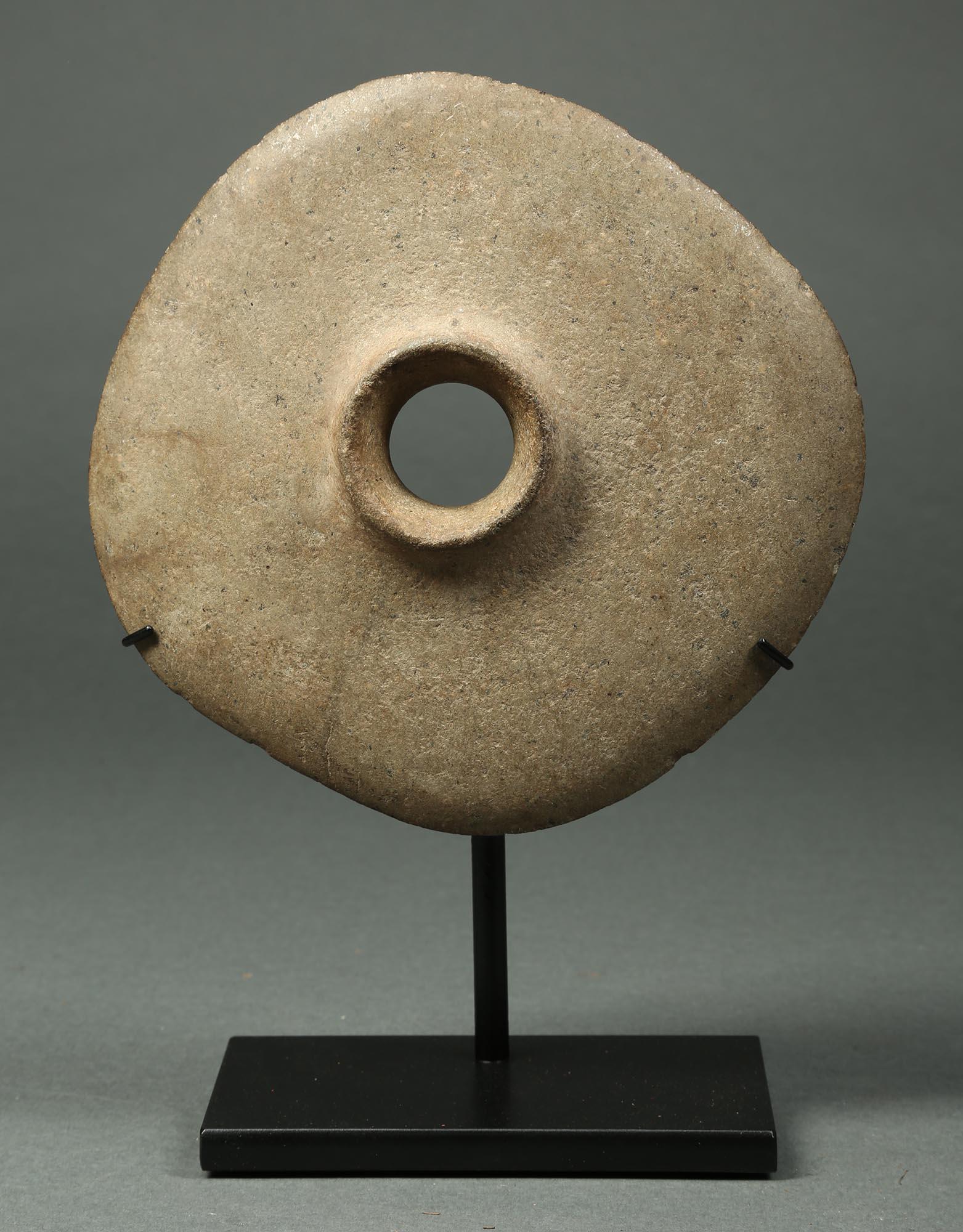 An early pre-contact ground stone disc mace head from New Guinea, with circular hole for attaching to a handle, simple raised shape around hole on one side, early 20th century or earlier. Very modern and contemporary form with a smooth feel to the