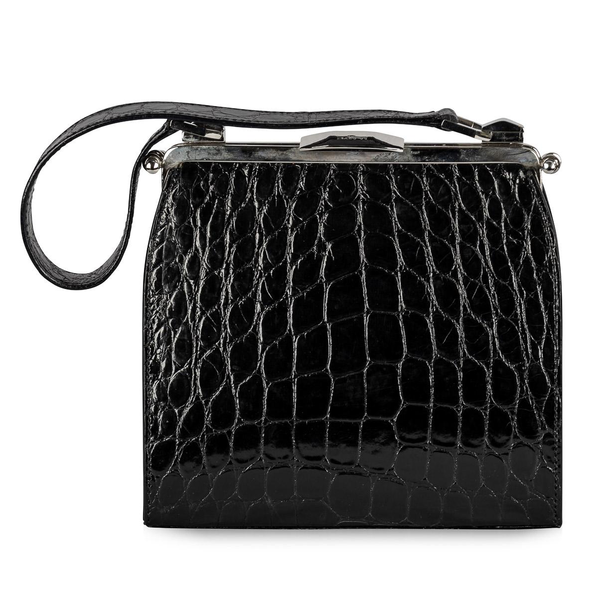 Crafted by Dotti in Roma, Italy during the early 21st Century, this handbag boasts black crocodile leather adorning both its exterior and handle. Palladium plated hardware throughout, from its clasp to the clam shell opening system, accentuates its