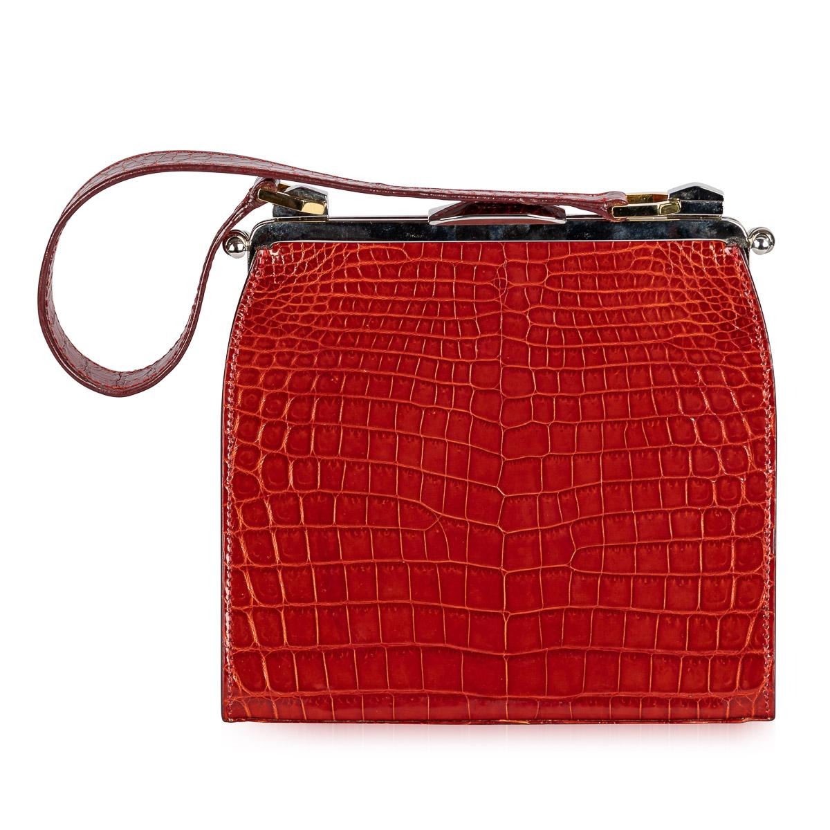 Crafted by Dotti in Roma, Italy during the early 21st Century, this handbag boasts red crocodile leather adorning both its exterior and handle. Gleaming gold and palladium plated hardware, from its clasp to the clam shell opening system, accentuates
