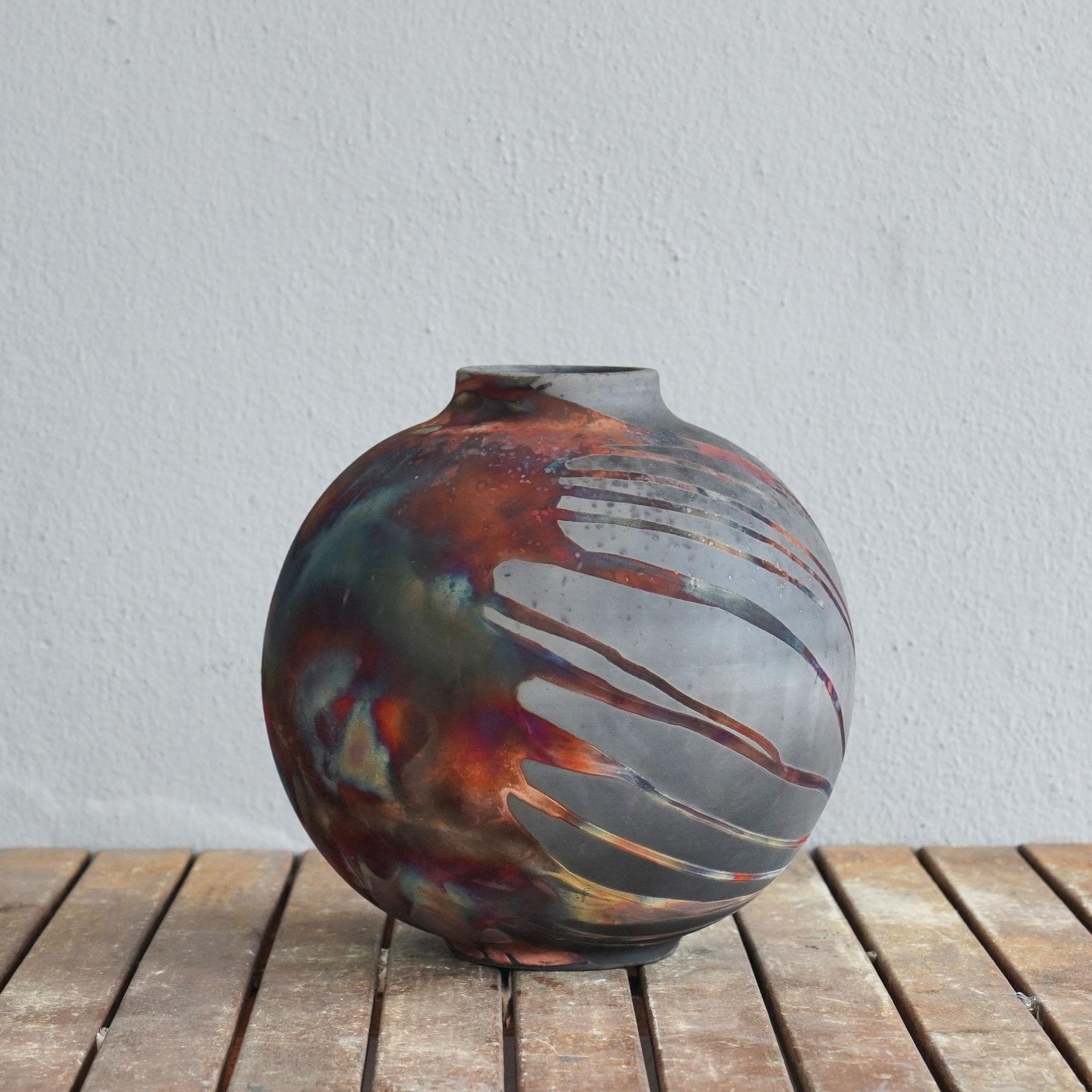 La serie di grandi vasi centrotavola cotti in Raku di RAAQUU.

Uno spettacolo ipnotico da ammirare non appena le patine arcobaleno catturano la tua attenzione.

Questo vaso a forma di globo è un pezzo rotondo e capiente prodotto con la tecnica Raku,