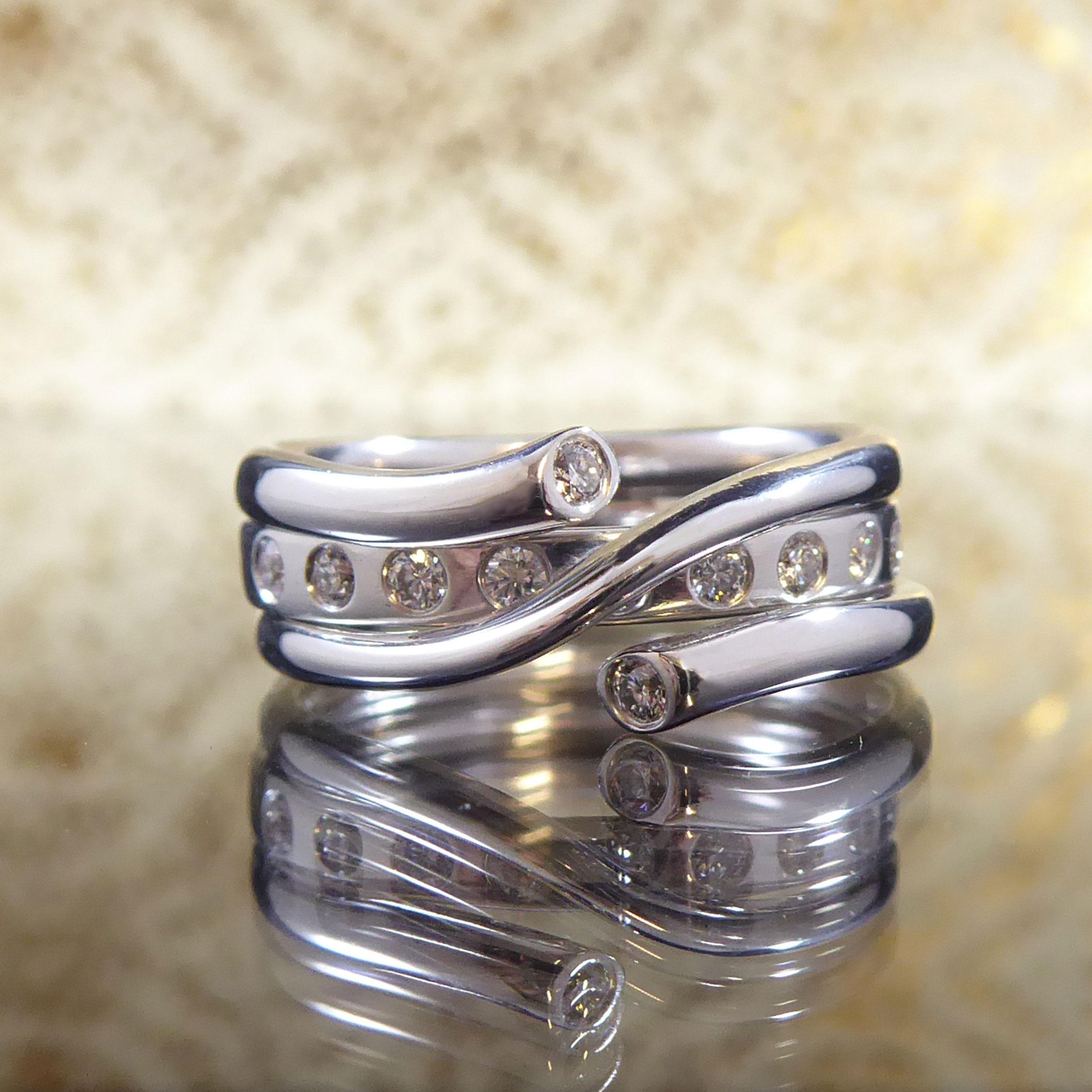 Aus dem Designhaus Georg Jensen haben wir einen gebrauchten Ring aus Weißgold und Diamanten aus der Magic Kollektion.  Der Ring besteht aus zwei Teilen: einem inneren D-förmigen Band, das mit neun Diamanten besetzt ist, die ein Gesamtkaratgewicht
