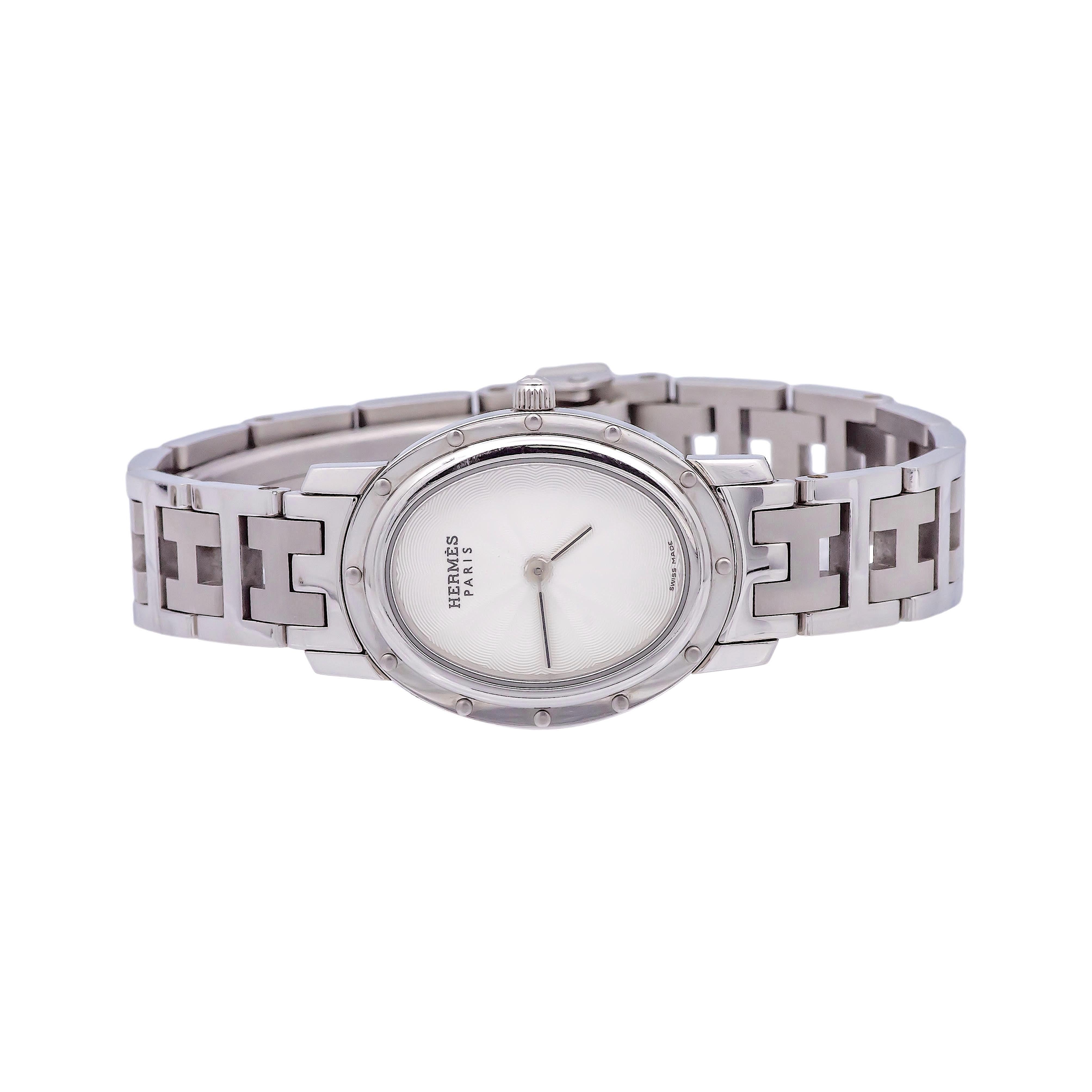 Pre-Owned Hermes Ladies watch from the Clipper collection finely crafted in stainless steel with an oval shape case and white silver dial with crown and analog display. Face measures 32.5mm x 22mm. Watch has a quartz movement and was made in