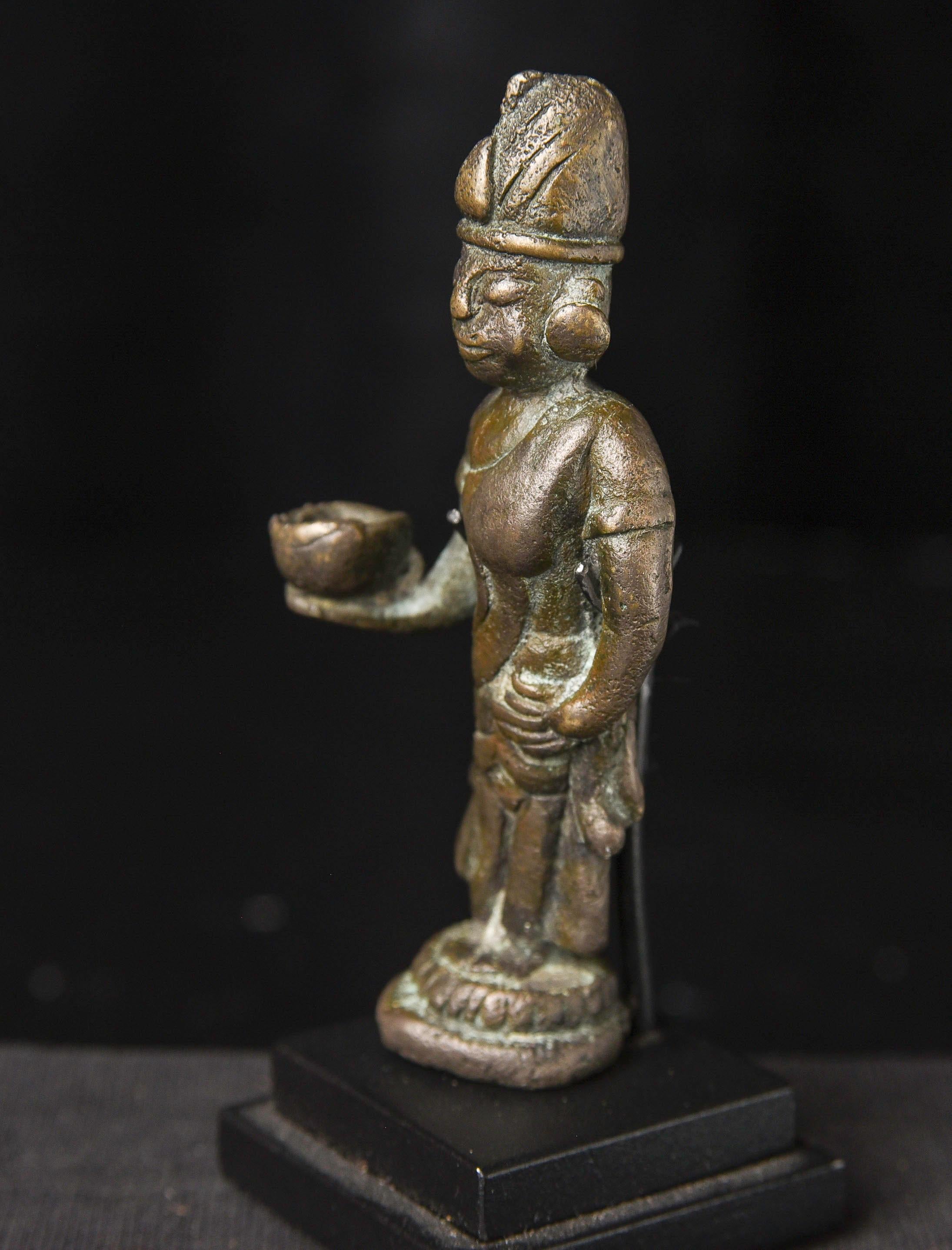 Excepcional figura antigua de bronce birmano, de más de 1.000 años de antigüedad, que representa a un personaje con atuendo tradicional de palacio, posiblemente representando a la realeza. La figura sostiene un cuenco de ofrendas, lo que sugiere una