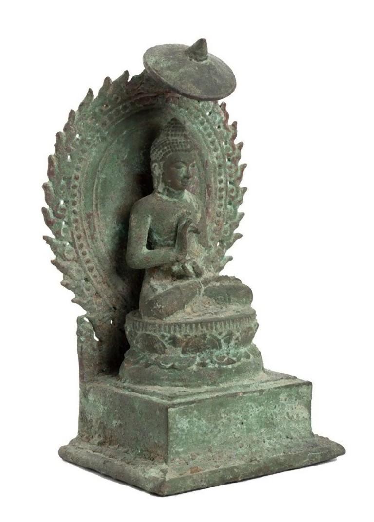 This bronze Throned Buddha is a precious bronze sculpture, realized in the Java Island, Indonesia, in 13th century.

The little smiling Buddha is sitting on a lotus flower base, supported by a roughly square section base, seated with the legs