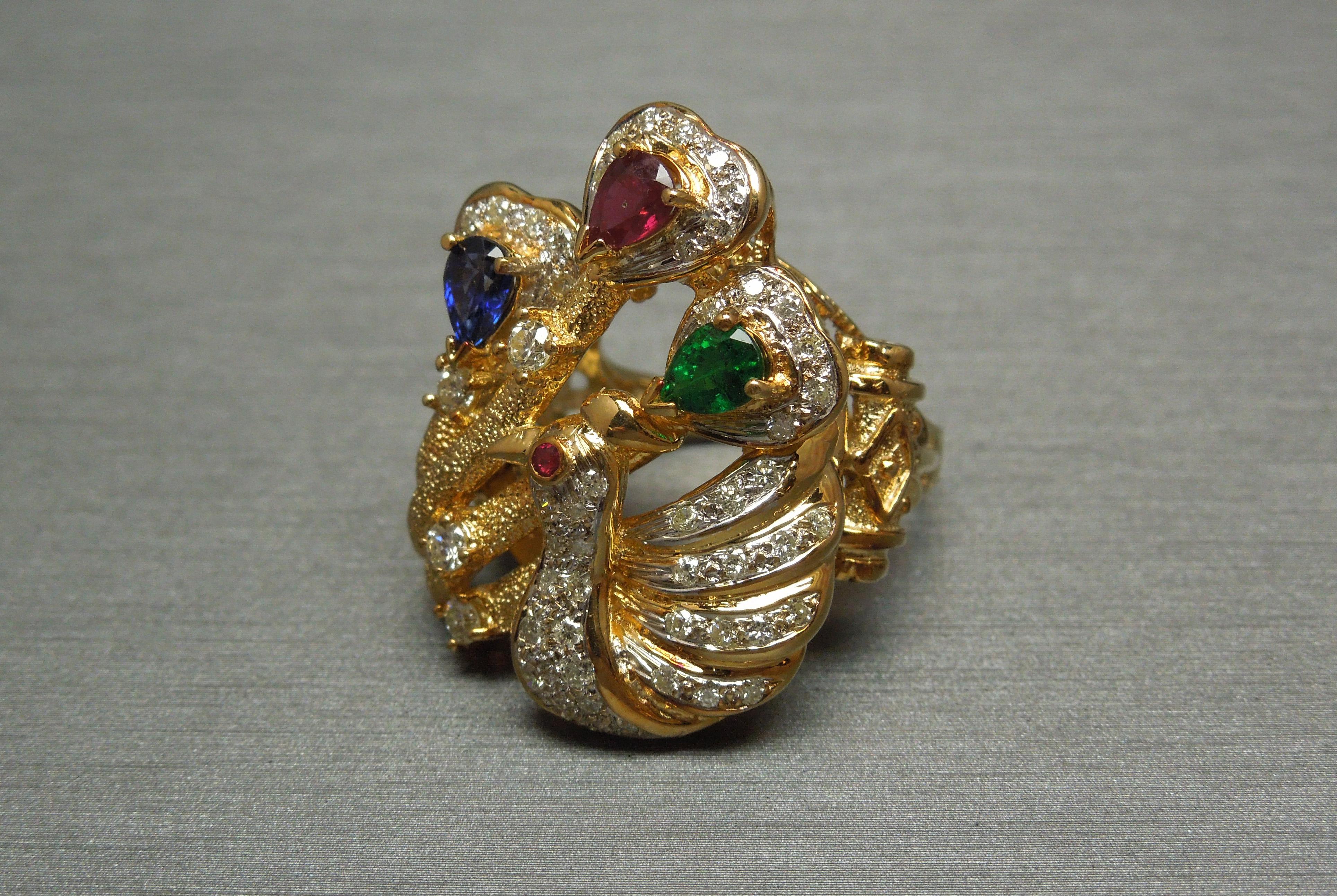 In a combination of 14KT & 18KT Gold, accented with exceptionally detailed Hand Engraving throughout. Featuring 3 Central Pear cut Brilliant Precious Gemstones - Ruby, Emerald, & Kashmir Sapphire - totaling 1.50 carats, each secured in three prongs.