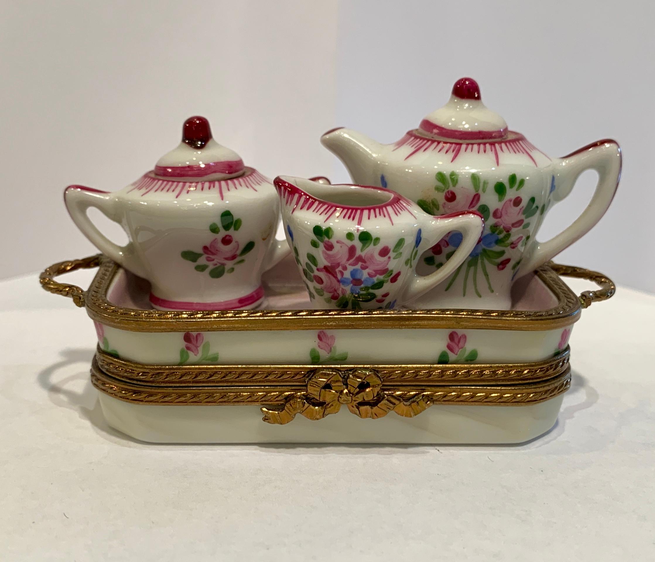 Very unusual, tiny Limoges porcelain miniature tea set is handmade and hand painted with a rose motif. Afixed tea set includes a teapot, lidded sugar bowl and creamer arranged on a beautiful serving tray. Tray opens to reveal a pair of afixed