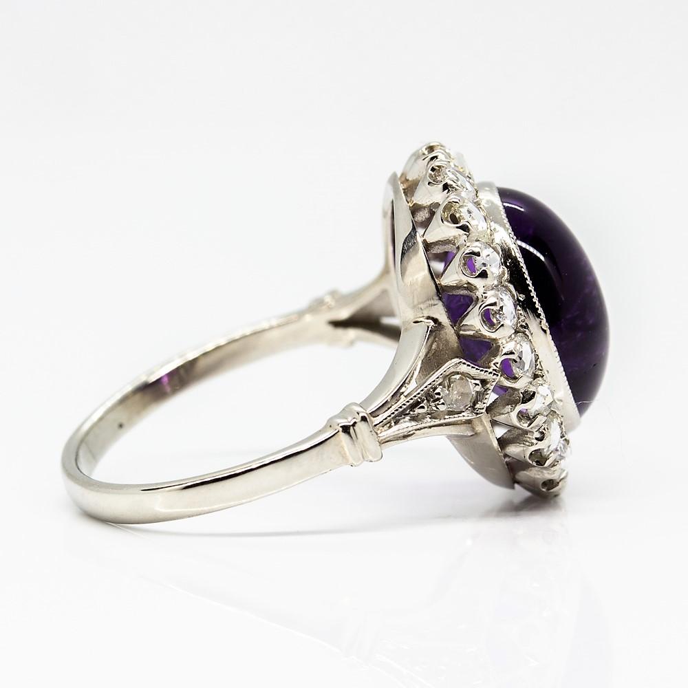 Crafted in solid platinum, this enticing ring is centered with a prominent natural cabochon oval cut amethyst that weighs 5ctw. 
The wonderful central gemstone is surrounded by a row of 22 glowing and flawless rose cut diamonds of I-VS2 quality