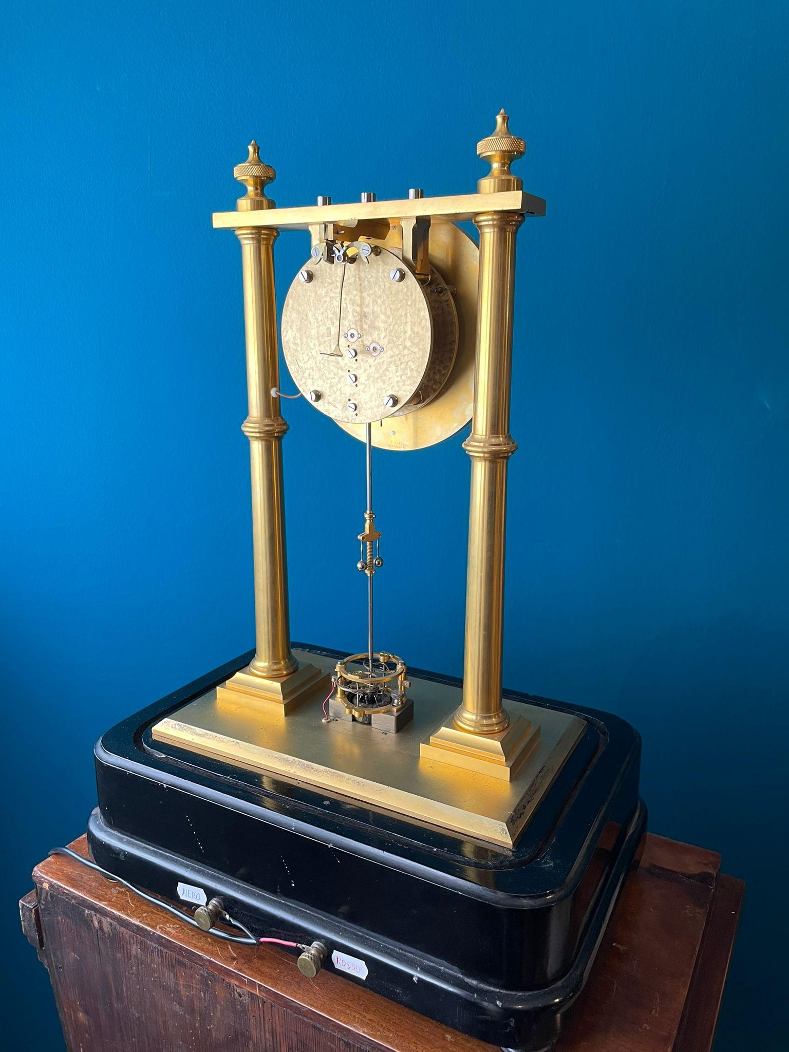 A very fine precision table regulator with a spectacular variant of an electric winding system.
Massive facetted gilt brass base, two massive gilt brass colums, in between vertical iron rod with spool, magnets, two contact wheels and governor for