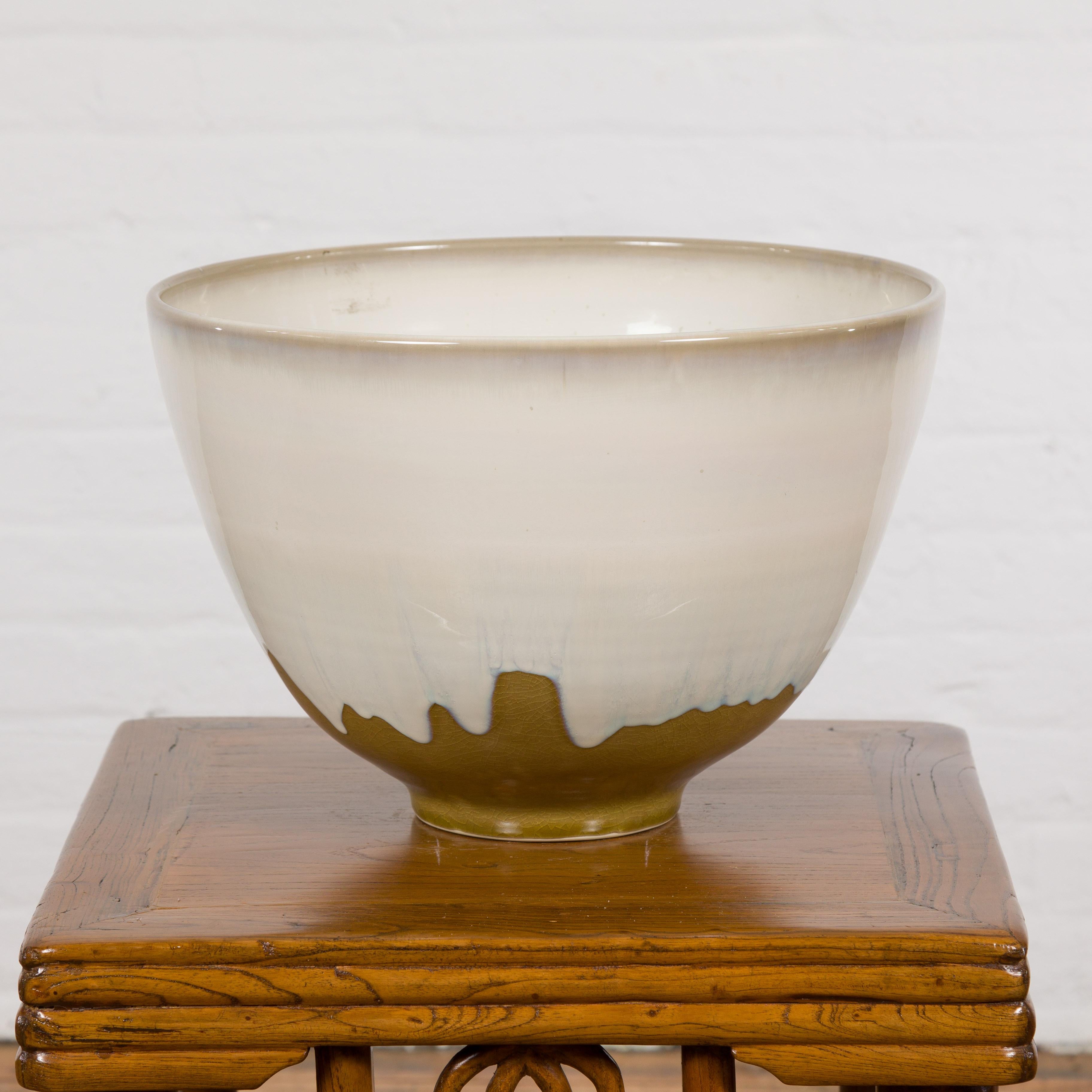 Un'ampia ciotola in ceramica con smalto bianco e base dorata. Questa ciotola in ceramica, lavorata artigianalmente, combina una forma elegante con uno smalto silenziosamente espressivo. Il corpo si svasa dolcemente verso l'esterno prima di