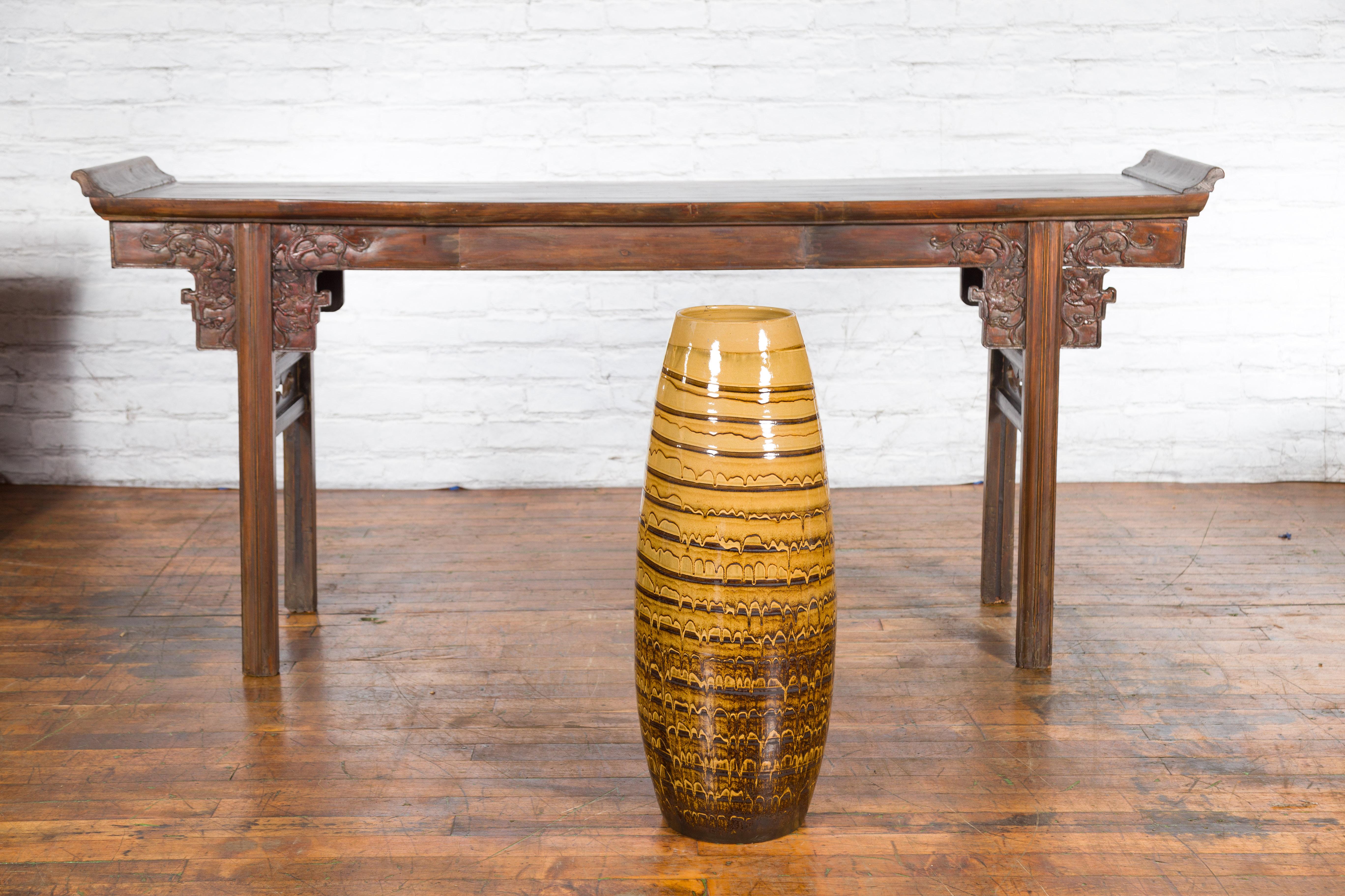 A contemporary Northern Thai ceramic vase from the Prem Collection, with dripping décor and slender silhouette. Charming our eyes with its pure lines and yellow and brown tones, this vase was born in Chiang Mai, northern Thailand. Showcasing an