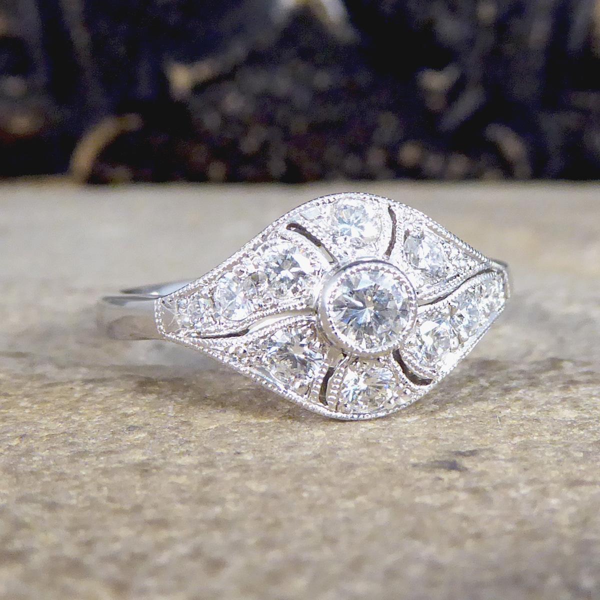 This stunning ring has been hand crafted and is new and never worn. It has been designed and carefully crafted to resemble an Art Deco style ring with a collar set Brilliant Cut Diamond in the centre with a milgrain edge surrounded by an array of