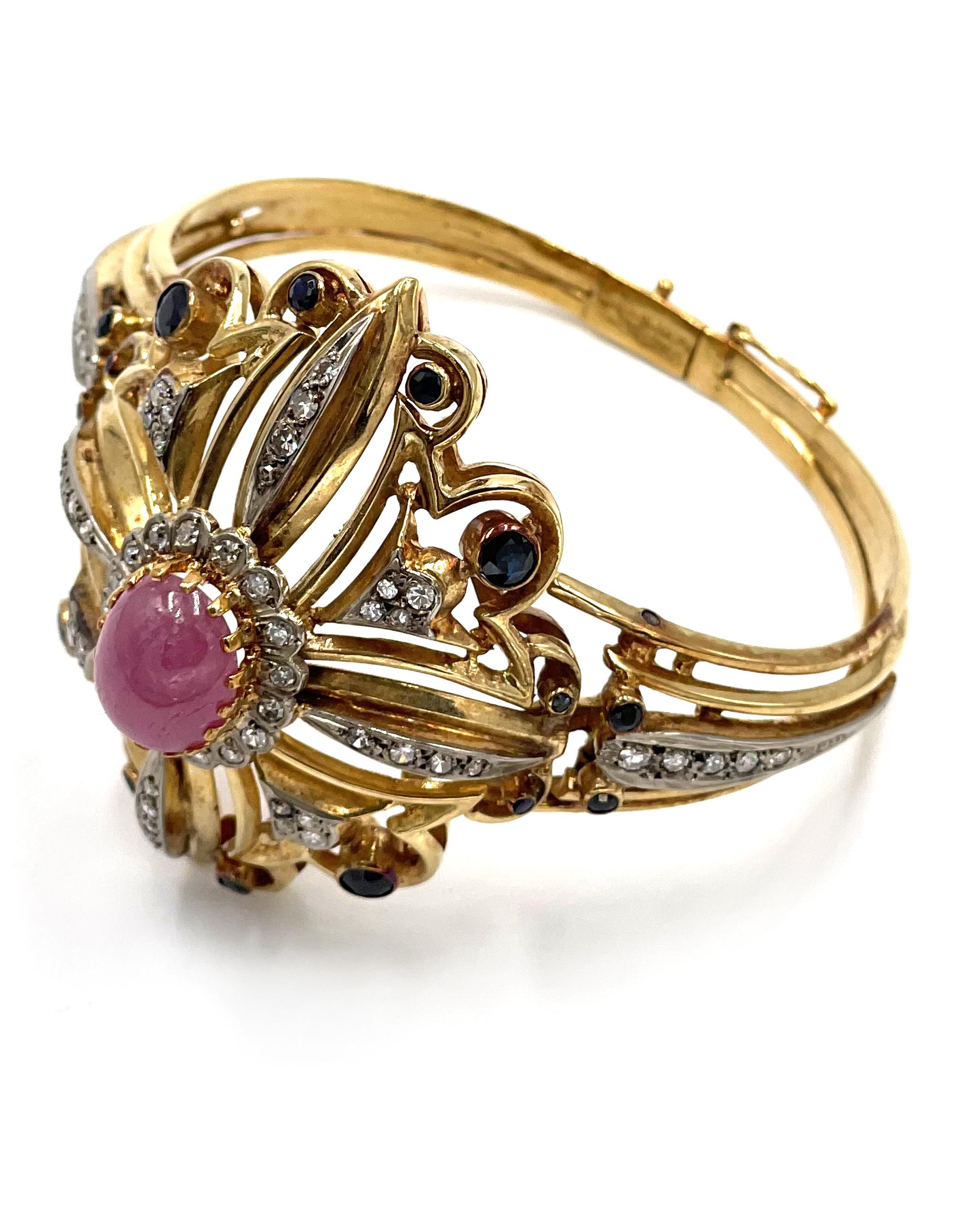 Pre owned vintage estate Ilias Lalaounis 18K yellow gold pink sapphire, blue sapphire and diamond hinged bangle bracelet.  The top center is prong set with one oval cabochon cut pink sapphire measuring approximately 12.75X10.0X4.7mm.  The pink