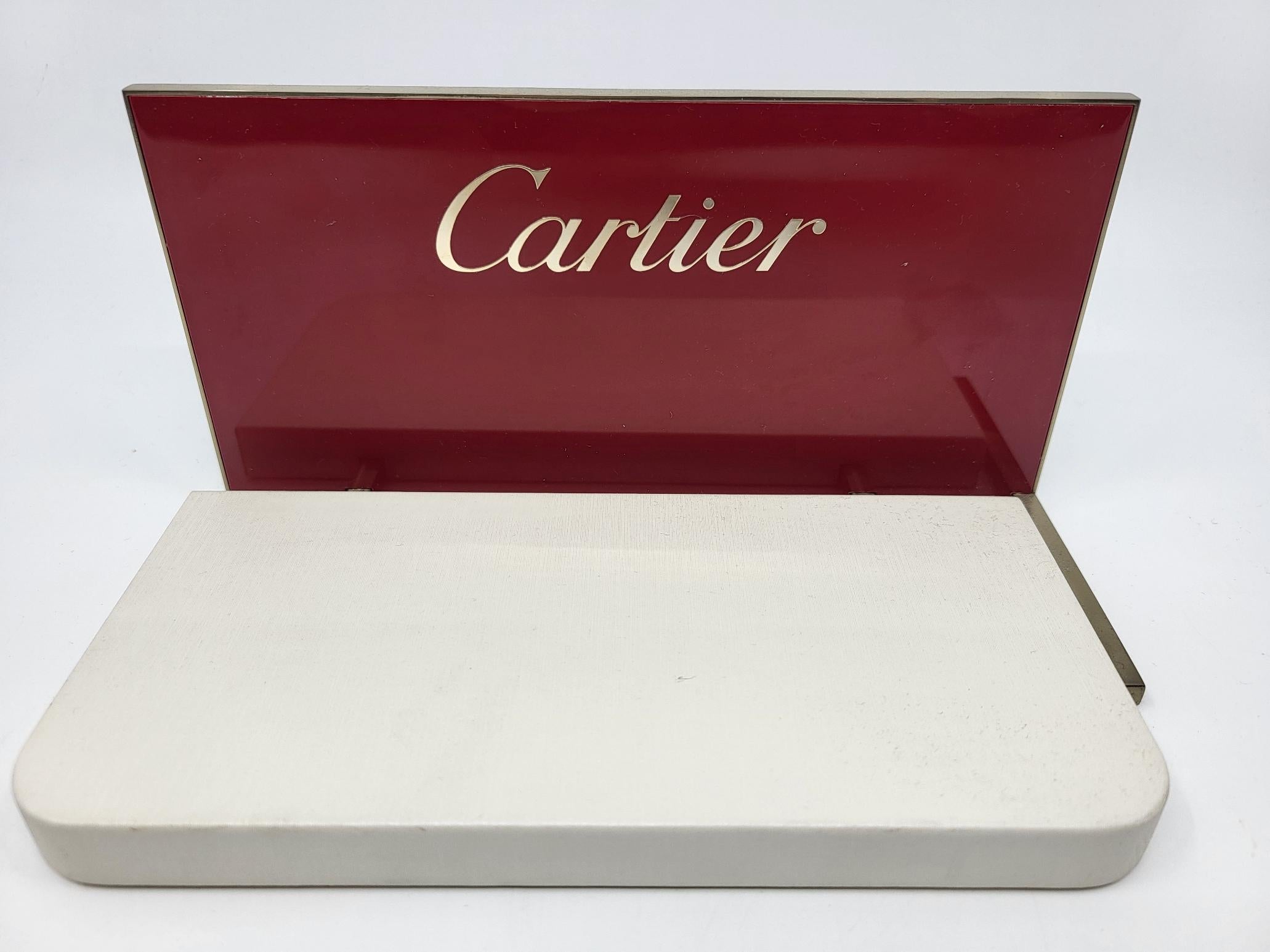 Descubre el refinamiento de la tienda Cartier, ideal para realzar tus joyas o monturas con un toque de elegancia. Este présentoir chic tiene una base blanca inmaculada y un panel frontal rojo, con el prestigioso logotipo de Cartier en letras doradas
