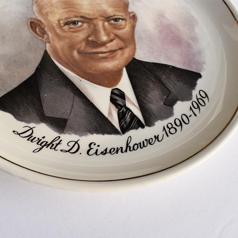 A round ceramic commemorative plate of President Dwight Eisenhower. The plate is circular, with gold detail around the edges, and a portrait of President Eisenhower in the center. Below, it reads 