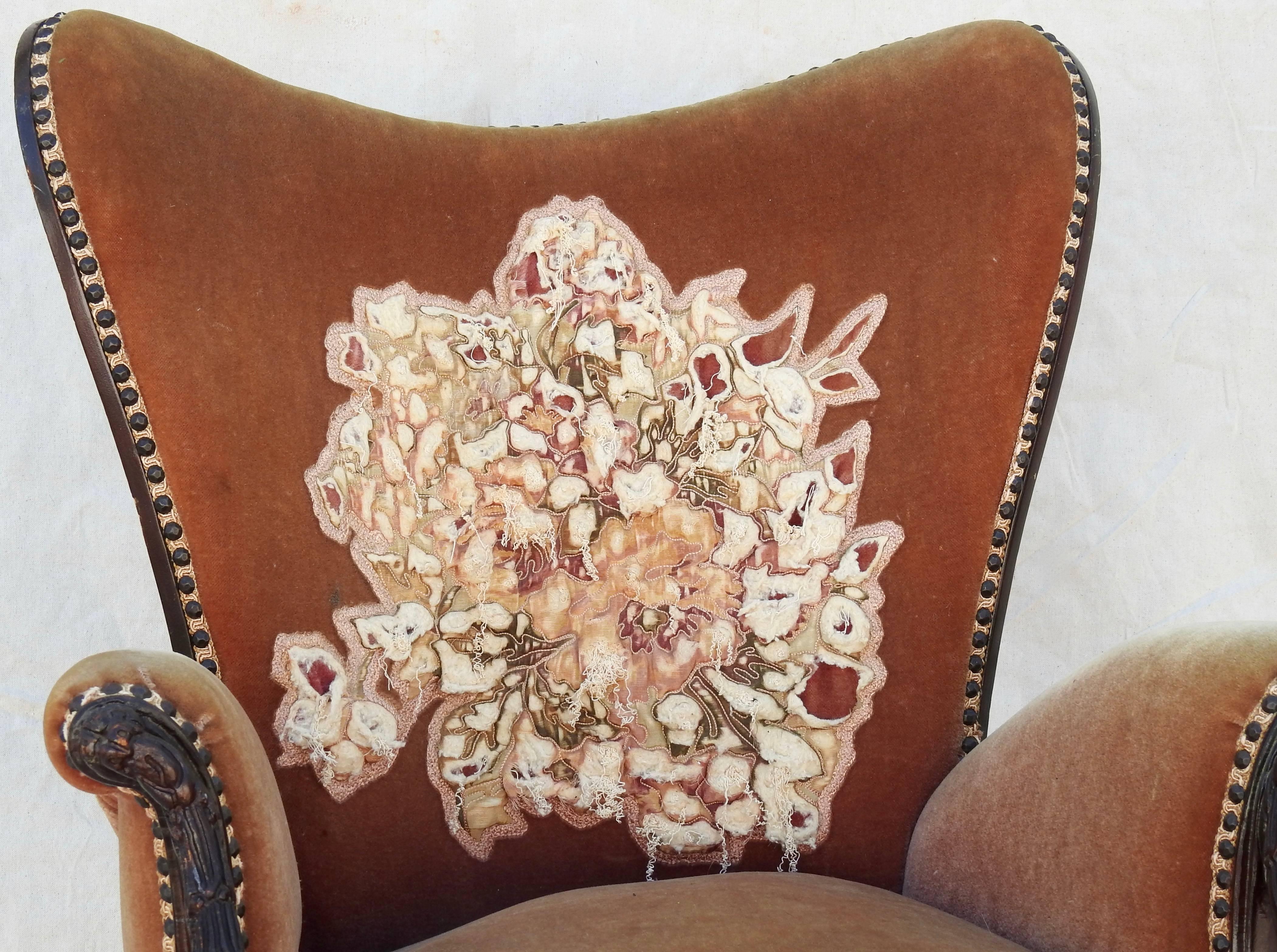 The wood carving on this wingback chair is stunning! The chair is upholstered in soft velvet and the back has an appliqued floral pattern with plenty of wear. The gimp trim is attached with hammered bronze tacks. The chair is attributed to belonging