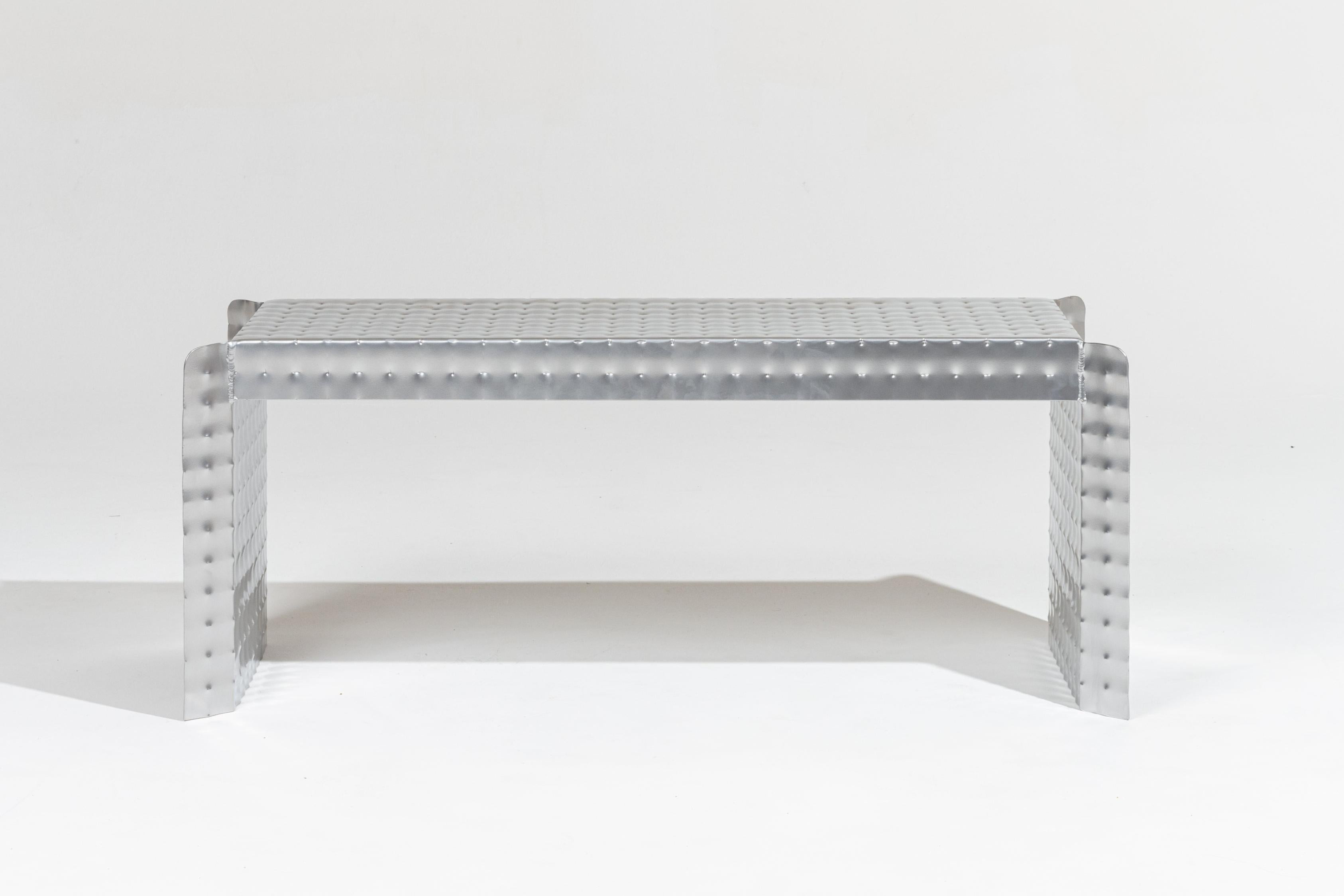 Banco de presión de aluminio de Tim Teven.
La deformación del metal mediante presión revela detalles técnicos fascinantes, así como nuevas cualidades visuales y táctiles.
El taburete y el banco Presión se fabrican con planchas de aluminio en las que
