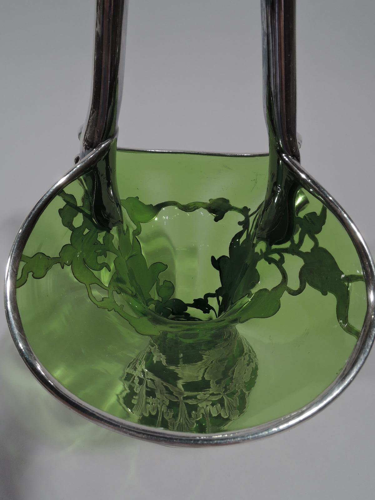 Pretty turn-of-the-century American Art Nouveau green glass basket with engraved silver overlay. Wide ovoid mouth with cylindrical body and spread foot. Silver V-form stationary handle with tooled ornamental mounts. Floral overlay in form of lush,