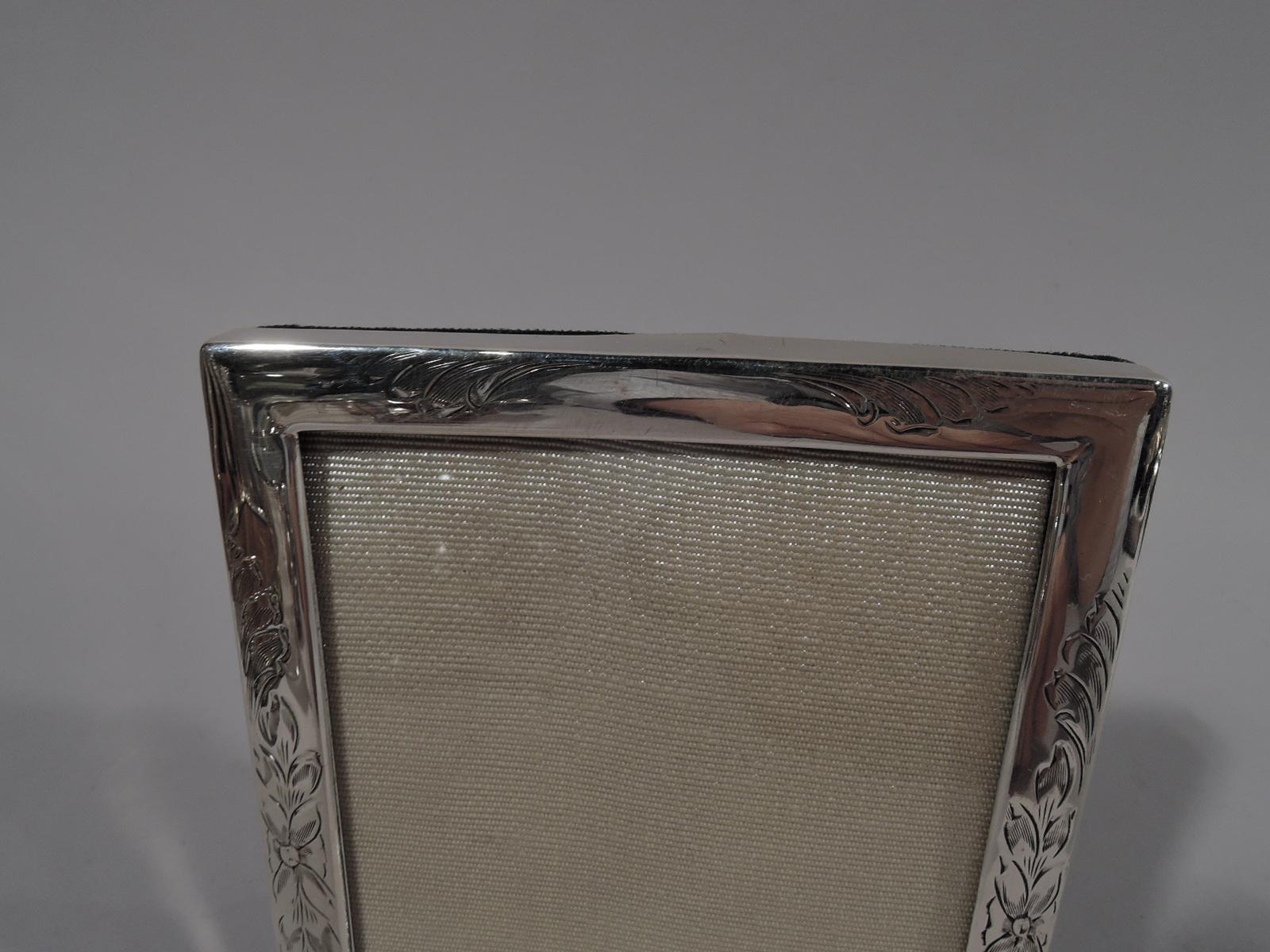 Pretty Art Nouveau sterling silver picture frame. Made by Scharling in Newark, circa 1910. Rectangular window engraved with feathery scrolls and flowers. With glass, silk lining, and velvet back and hinged support for portrait (vertical) display.