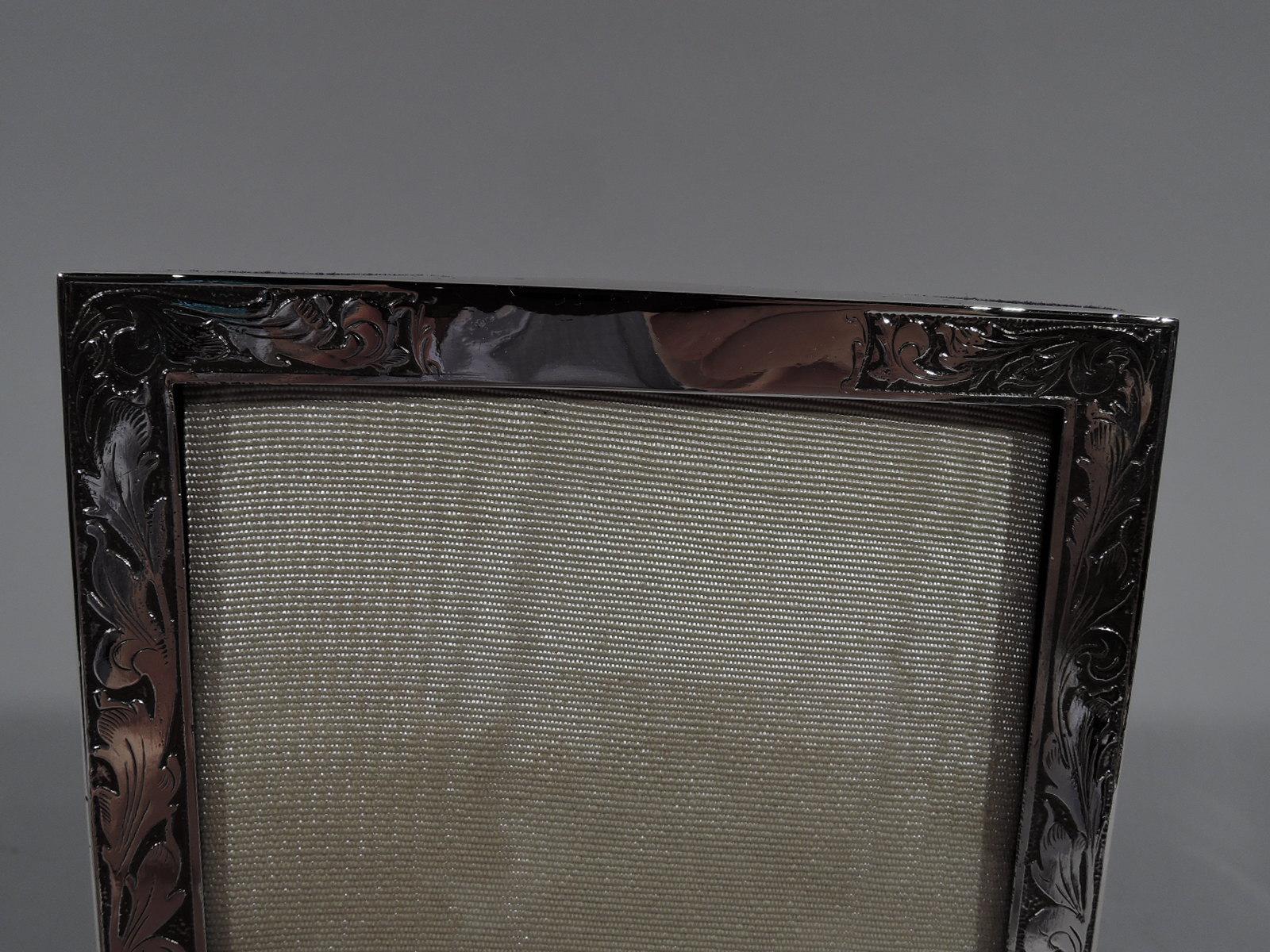 Pretty turn-of-the-century American Art Nouveau sterling silver picture frame. Rectangular window in flat surround with acid-etched scrolling leaves. Top center vacant. With glass, silk lining, and velvet back and hinged support. For portrait