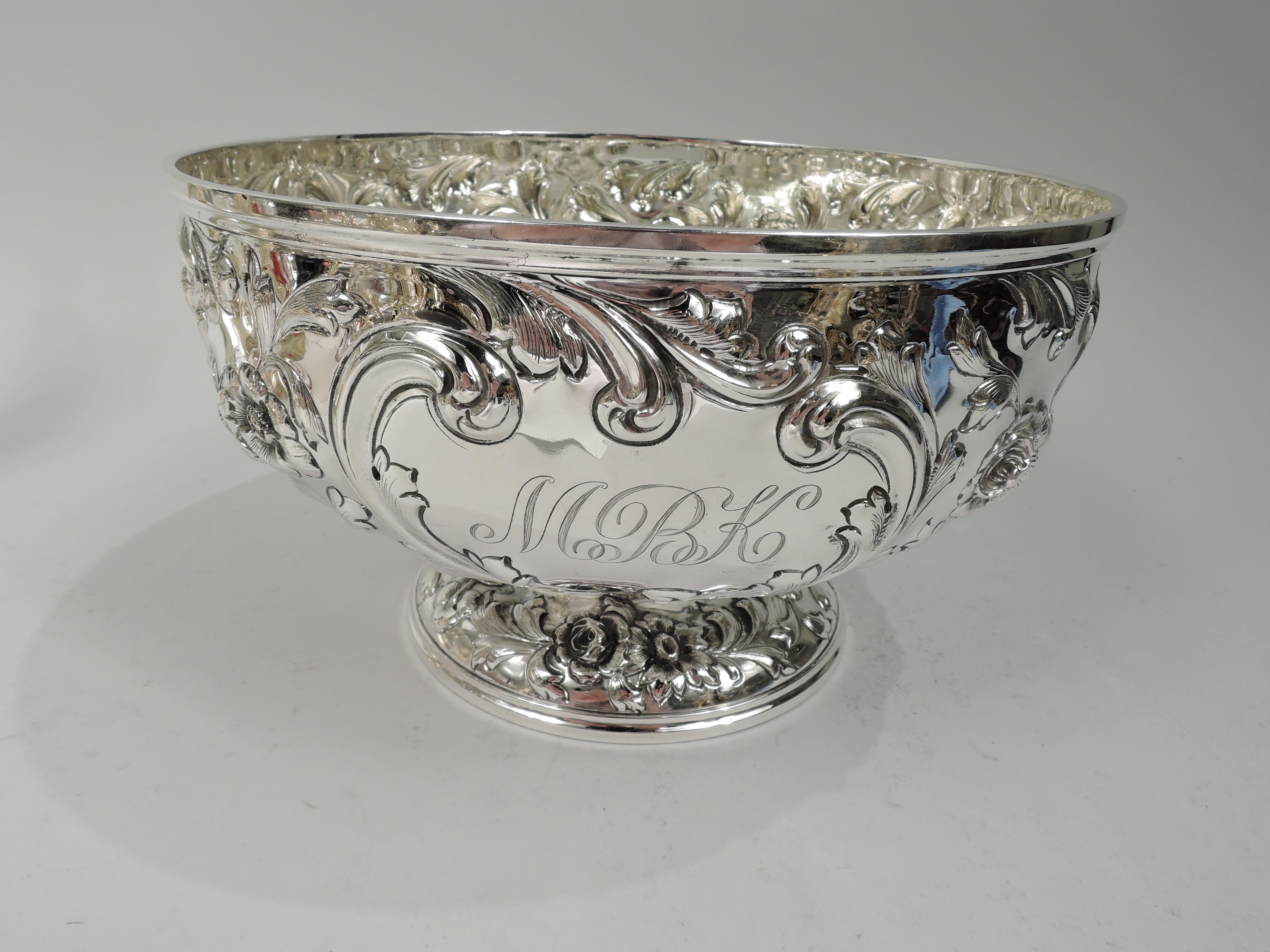 Turn-of-the-century sterling silver centerpiece bowl. Made by Davis & Galt in Philadelphia. Round and curved on raised foot. Repousse ornament. Scattered flowers and leaves, and leafing scrolled frame engraved with 3-letter script monogram. Floral