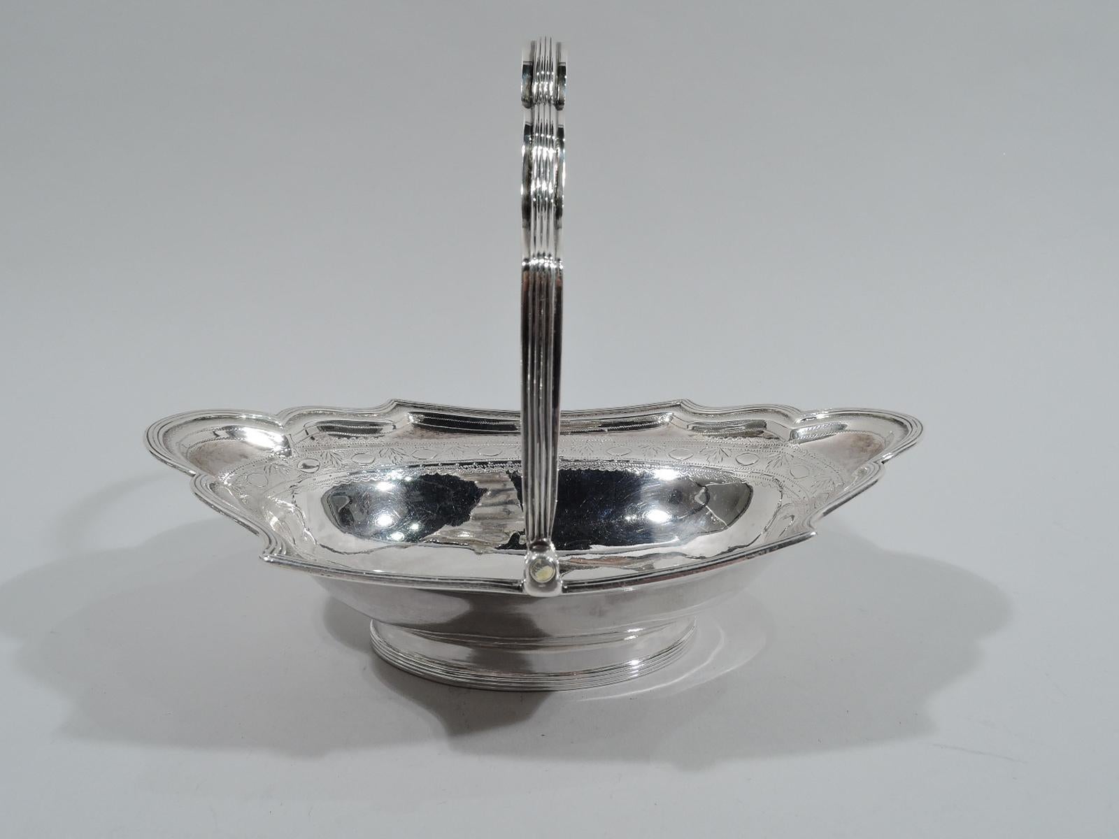 Pretty English Georgian sterling silver basket, 1795. Oval bowl with curvilinear shoulder, same swing handle, and oval foot. Engraved ornamental border. Reeding. Worn marks including London assay stamp. 

Dimensions: H (with handle) 5 3/4 x W 6