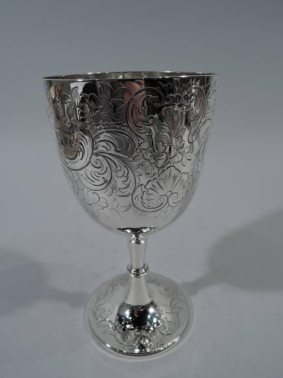 Victorian sterling silver goblet. Made by Henry Holland in London in 1862. Tapering and curved bowl on knopped and tapering stem and raised foot. Leaves, flowers, and shells engraved on bowl. Feathery scrolled frame (vacant). Same ornament on foot