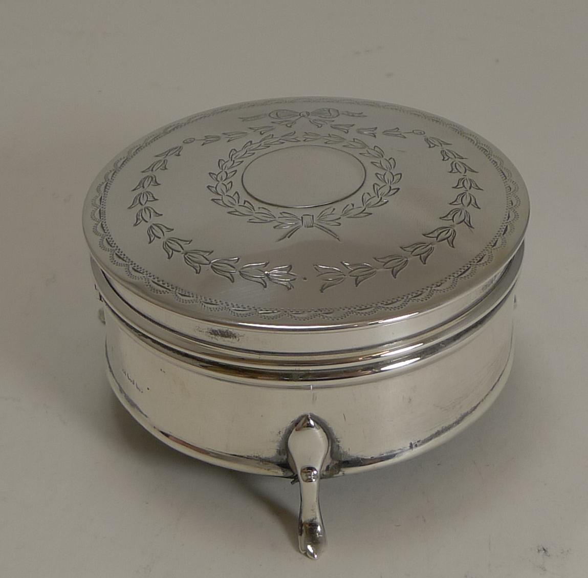 A wonderful pretty circular jewelry box standing on three elegant legs.

The hinged lid is engraved with acanthus leaf garlands tied with ribbon and bows. The lid fits well and once opened reveals an attractive deep pink / red silk.

The silver