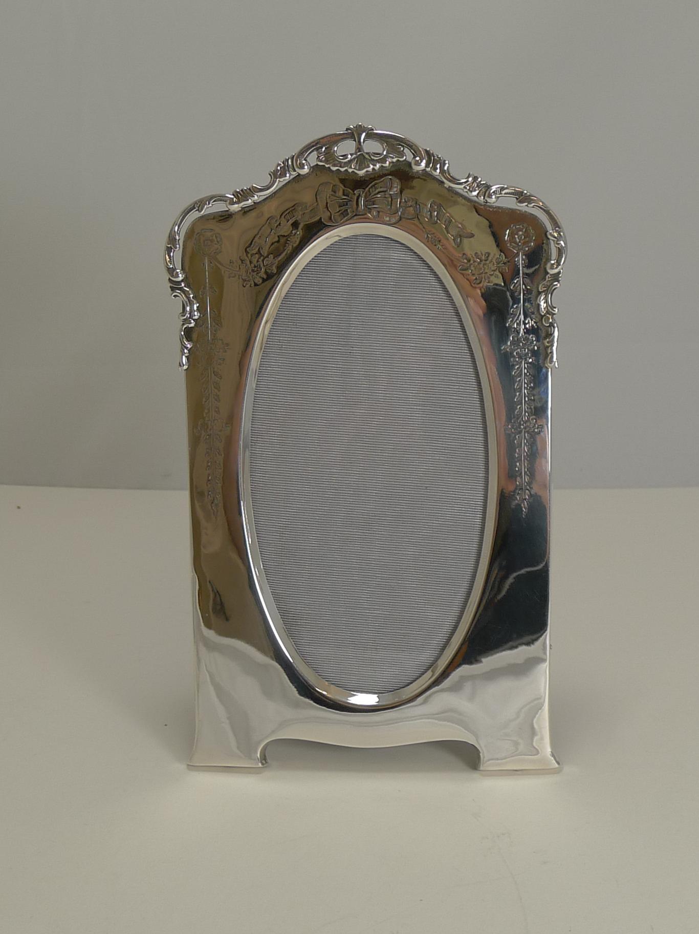 A really stunning Edwardian photograph frame made from English sterling silver on a solid oak backing with integral folding easel stand.

The beautifully shaped frame is topped with a shaped cast border with pierced or reticulated detail and hand
