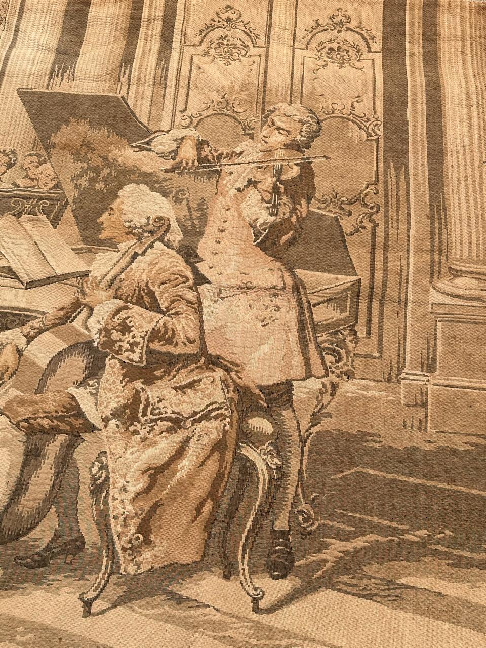 Eleva tu espacio con un impresionante tapiz antiguo de estilo Aubusson de principios del siglo XX. Meticulosamente tejida en un telar jacquard con una mezcla de lana y algodón de lujo, esta obra maestra te transporta a un concierto de personajes