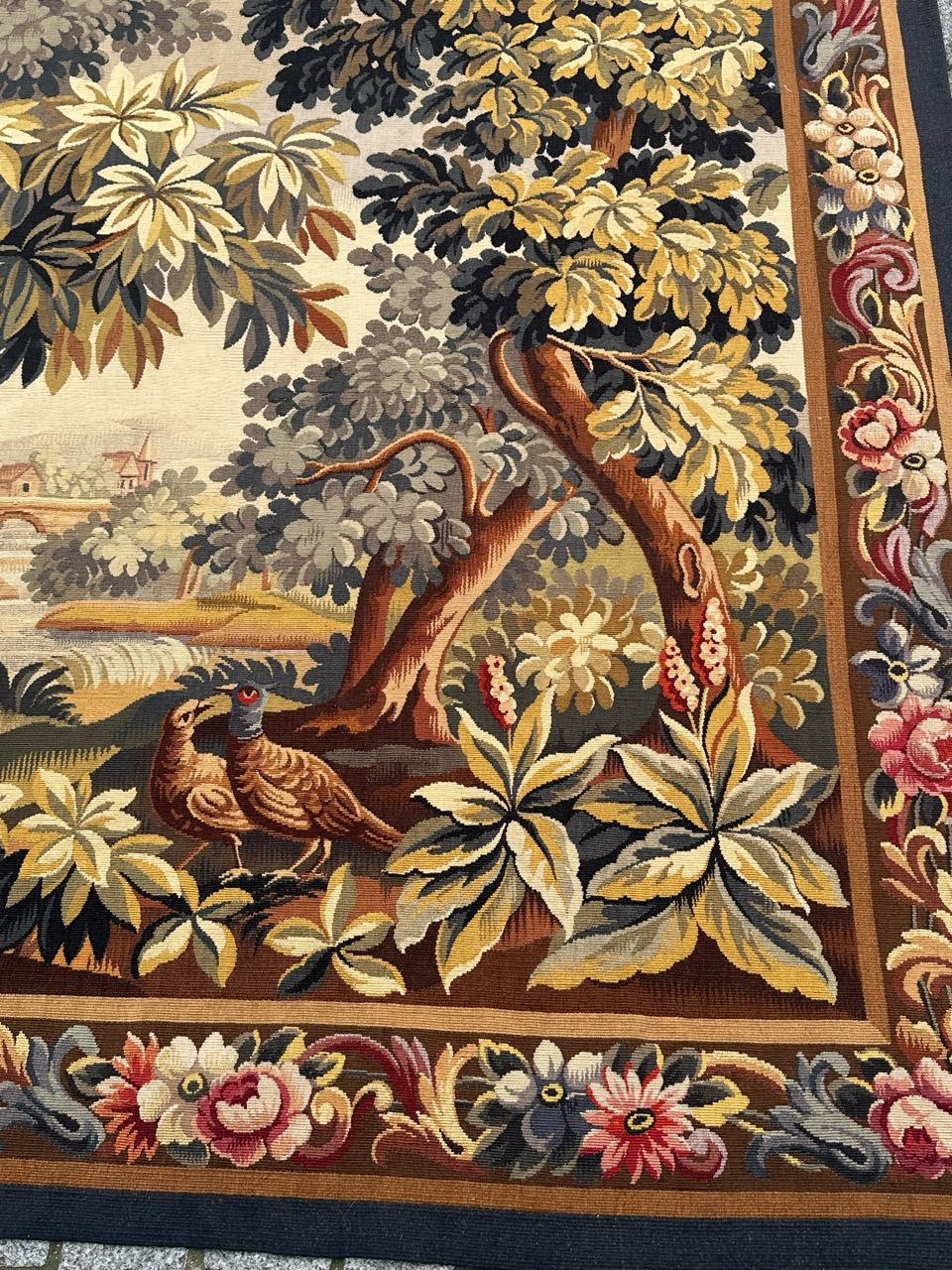 Precioso tapiz antiguo francés de Aubusson con una vista de la naturaleza en el bosque, con pájaros, árboles y un río. Se ven, más allá, casas de pueblo. Con bonitos colores naturales en tonos amarillo, verde, rosa, naranja, morado y marrón, tejida