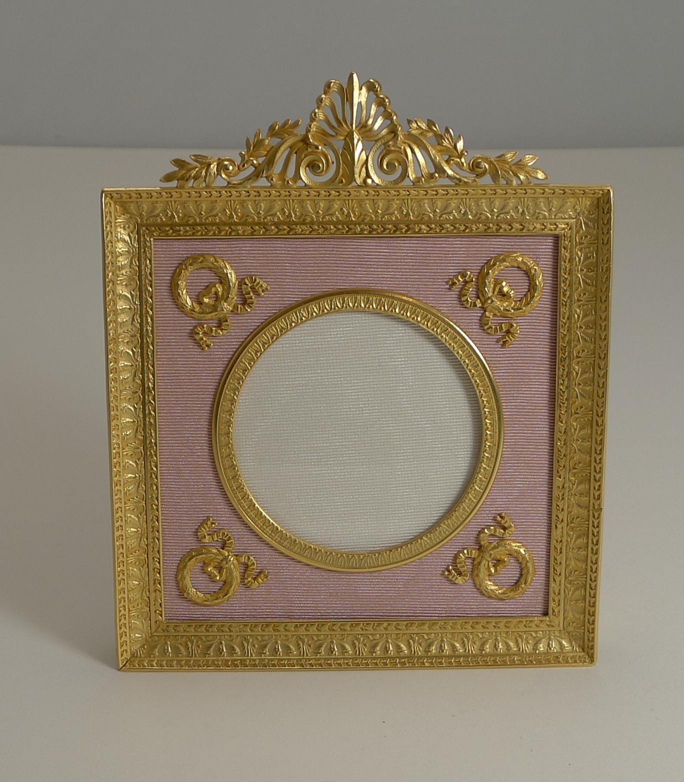 A fabulous late 19th-early 20th century photograph frame, French in origin and made from Ormolu, gold over bronze.

The circular aperture is surrounded by four gilded wreathes mounted on a pink taffeta.

Dating to circa 1900, it remains in