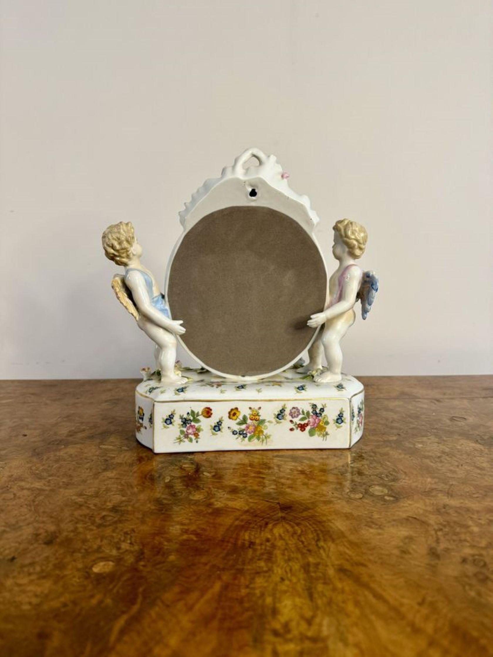 Pretty antique porcelain dressing table mirror, having an oval shaped mirror to the centre flanked by two cherubs, raised on a shaped rectangular base encrusted with beautiful flowers in pink, green, blue and yellow colours within gilded