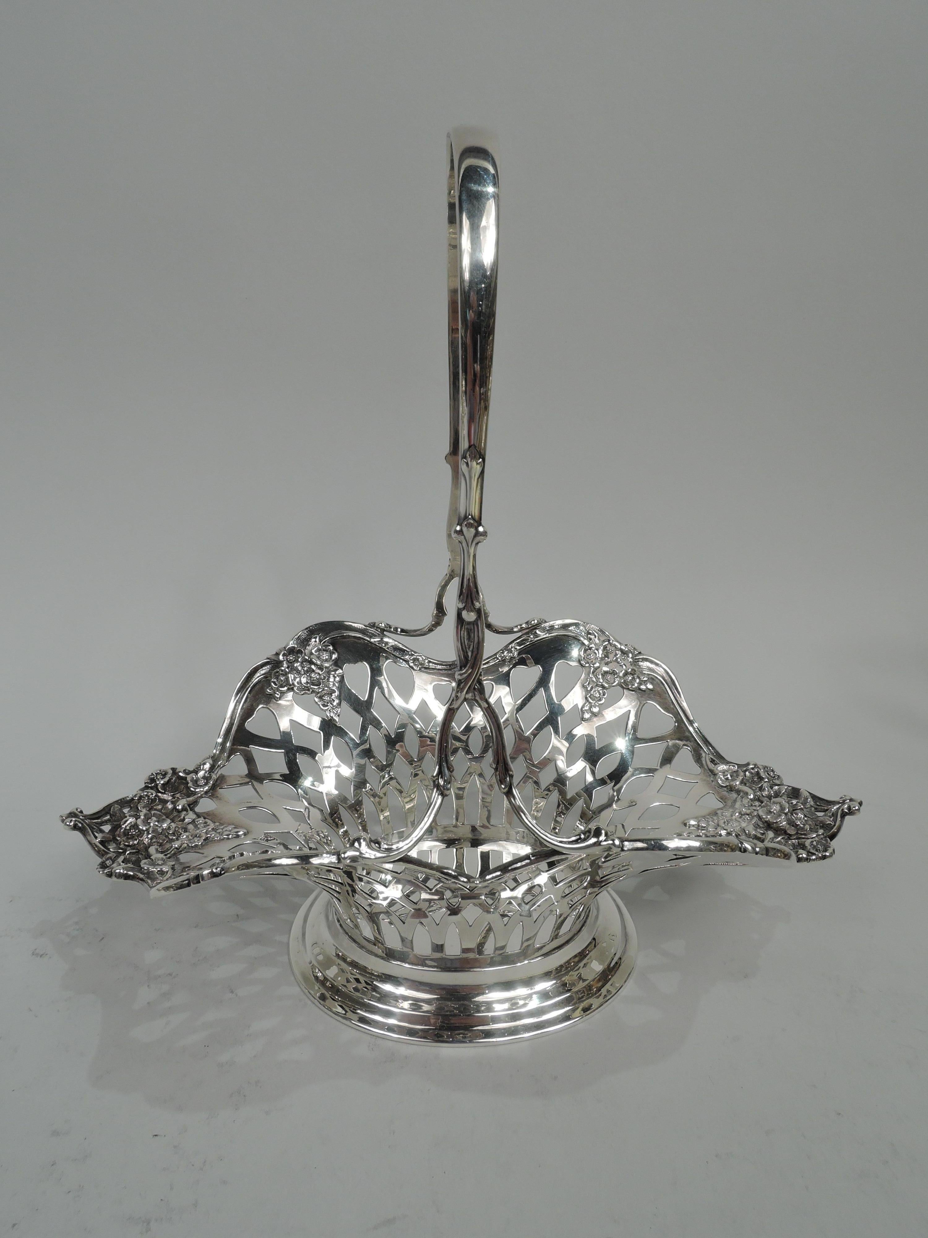 Pretty Edwardian sterling silver basket. Made by Tiffany & Co. in New York. Solid oval well and open weave-style sides with clusters of applied pendant flowers. Ends splayed. Scrolled rim. Tall and fixed c-scroll handle with entwined and split