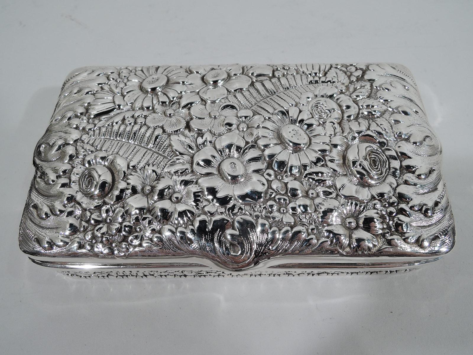 Pretty sterling silver box. Made by Tiffany & Co. in New York. Rectangular with curved corners and hinged cover. Cover top has dense floral repousse as does box sides. Interior gilt washed. Box interior partitioned. Compact and tactile. Fully marked