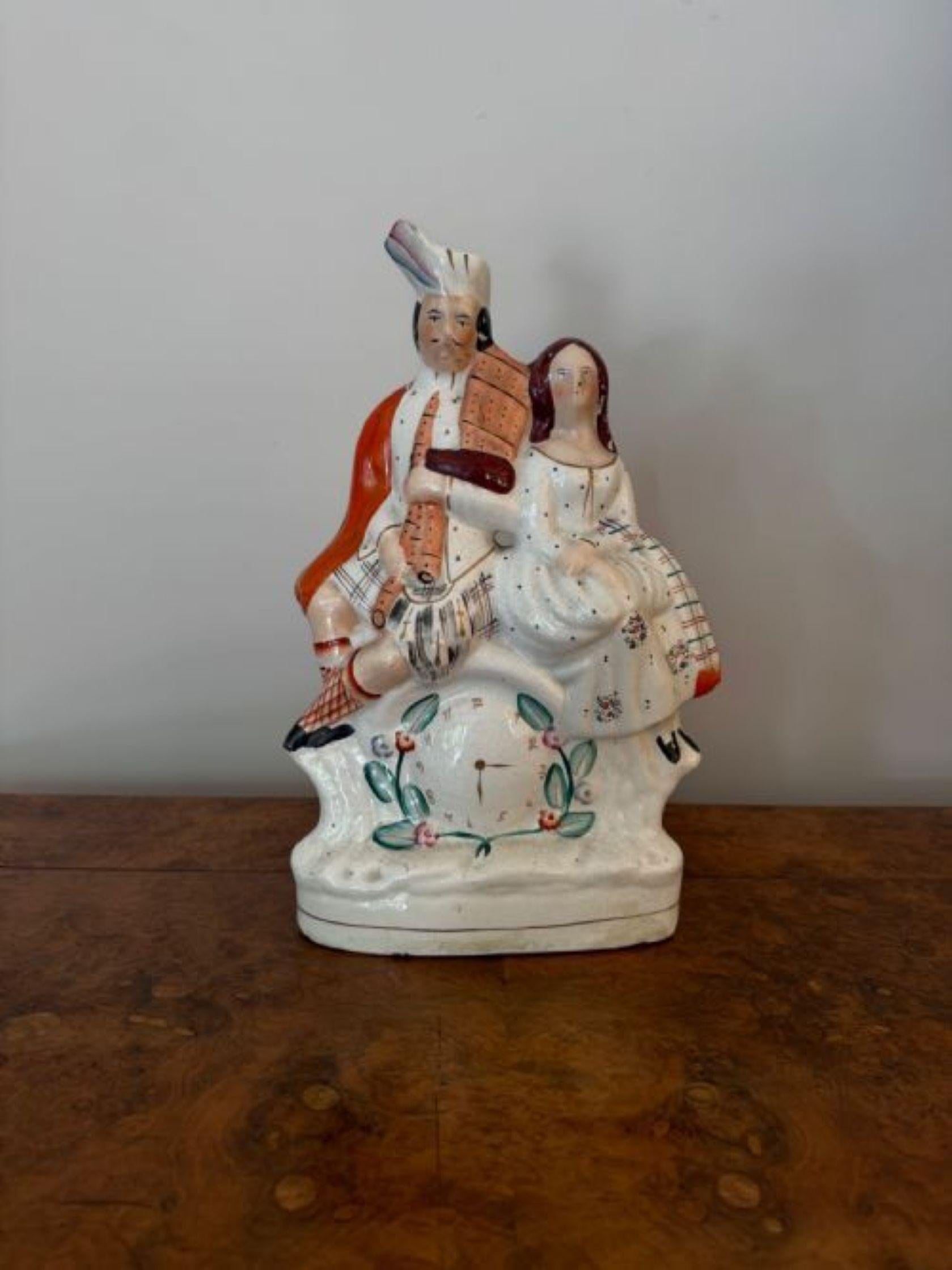 Hübsche große viktorianische Staffordshire-Figur eines Paares in sitzender Position, der Herr in traditioneller schottischer Hochlandkleidung mit Schottenrock, Schärpe und Federhaube, der einen Dudelsack mit dem  Neben ihm sitzt eine Dame in einem