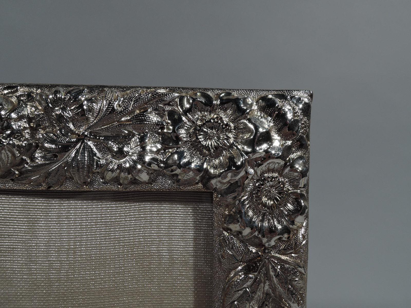 Beautifully ornate sterling silver picture frame. Made by Stieff in Baltimore in 1925. Rectangular window and repousse floral surround with abundant blooms. Interlaced script monogram engraved on rail top. A great piece by a premier regional maker.