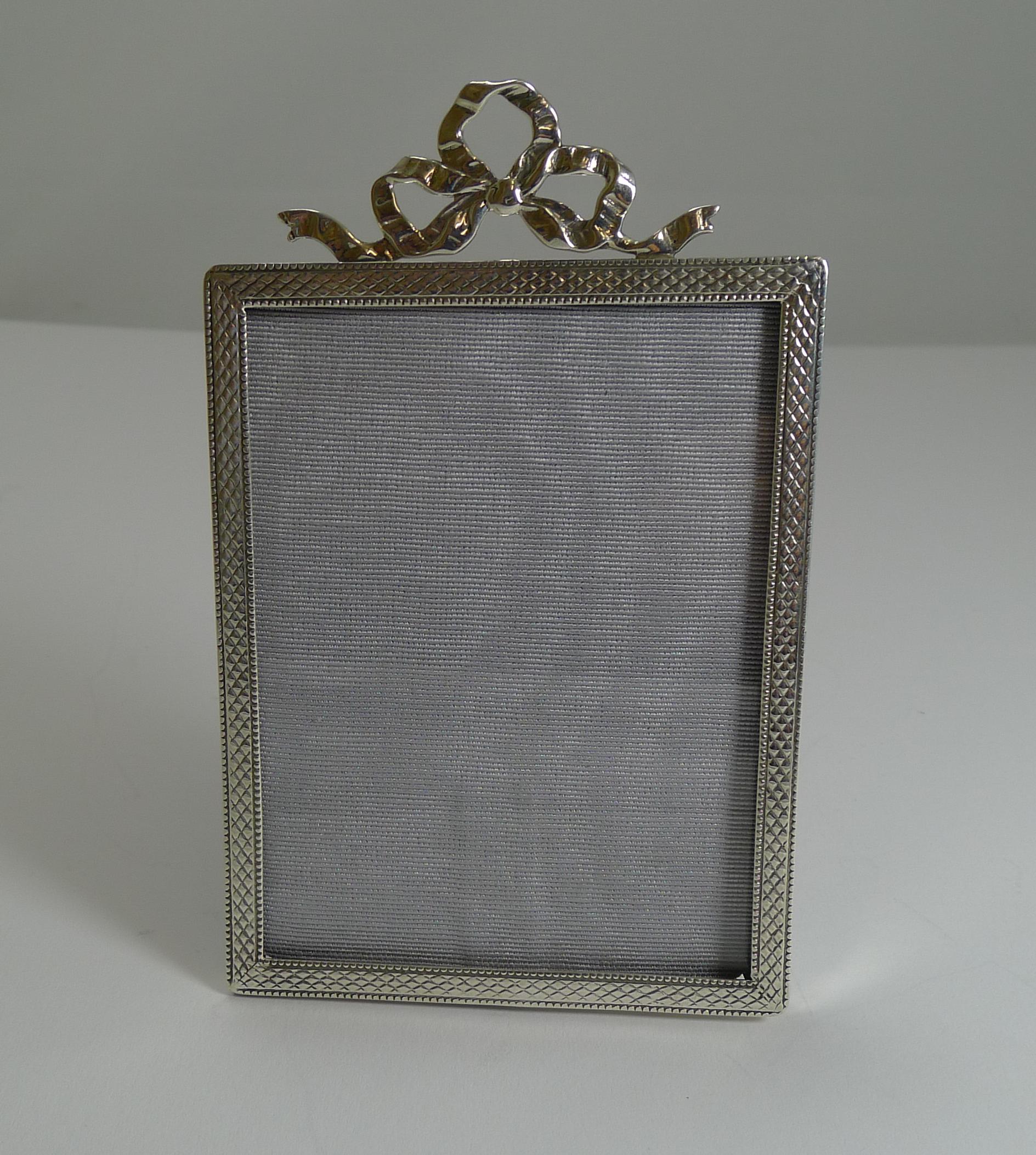 Pretty as a picture, this English sterling silver photograph frame approaches 100 years old with a full hallmark for Birmingham 1920.

The frame is beautifully decorated with a pretty engine-turned design and topped with a stunning cast ribbon and