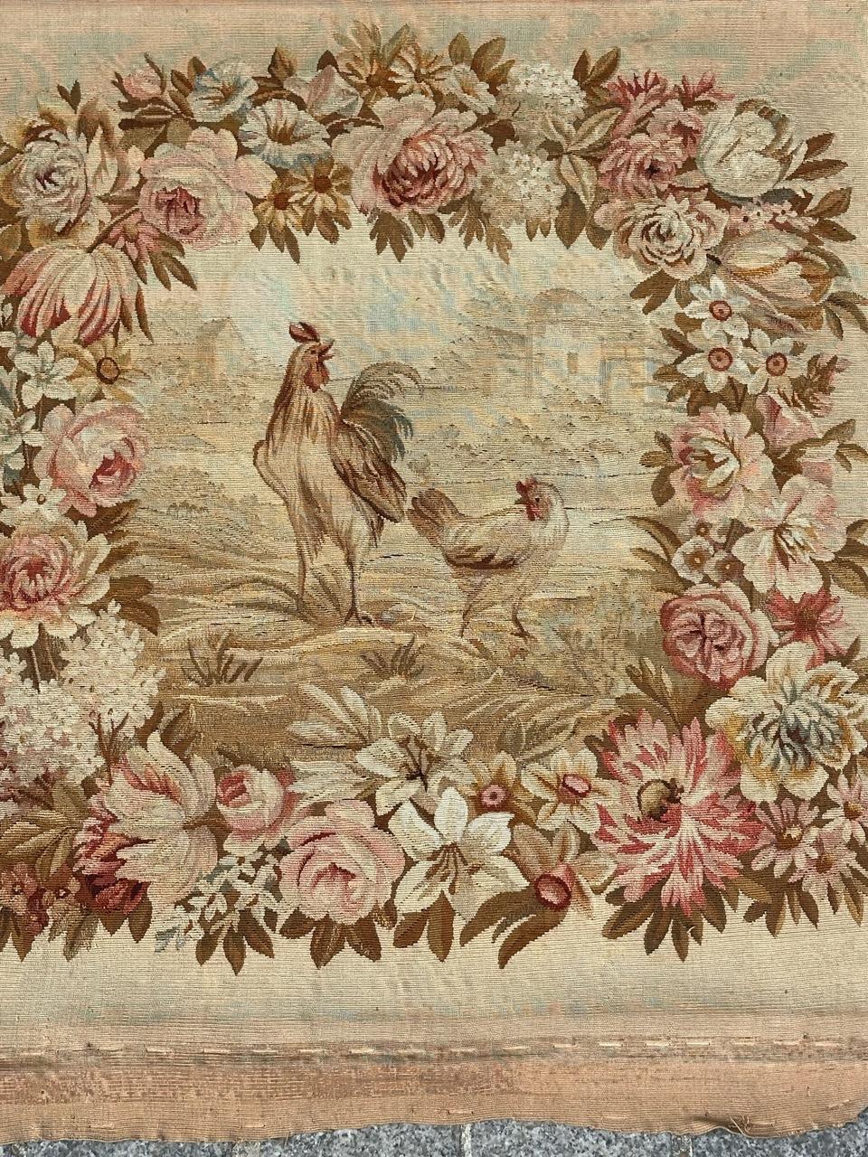 Un arazzo Aubusson molto bello e raffinato, con un bel disegno che presenta  una gallina e un gallo della fattoria, circondati da una striscia di fiori, con bellissimi colori naturali chiari nelle tonalità del rosso, verde, giallo, marrone e beige,