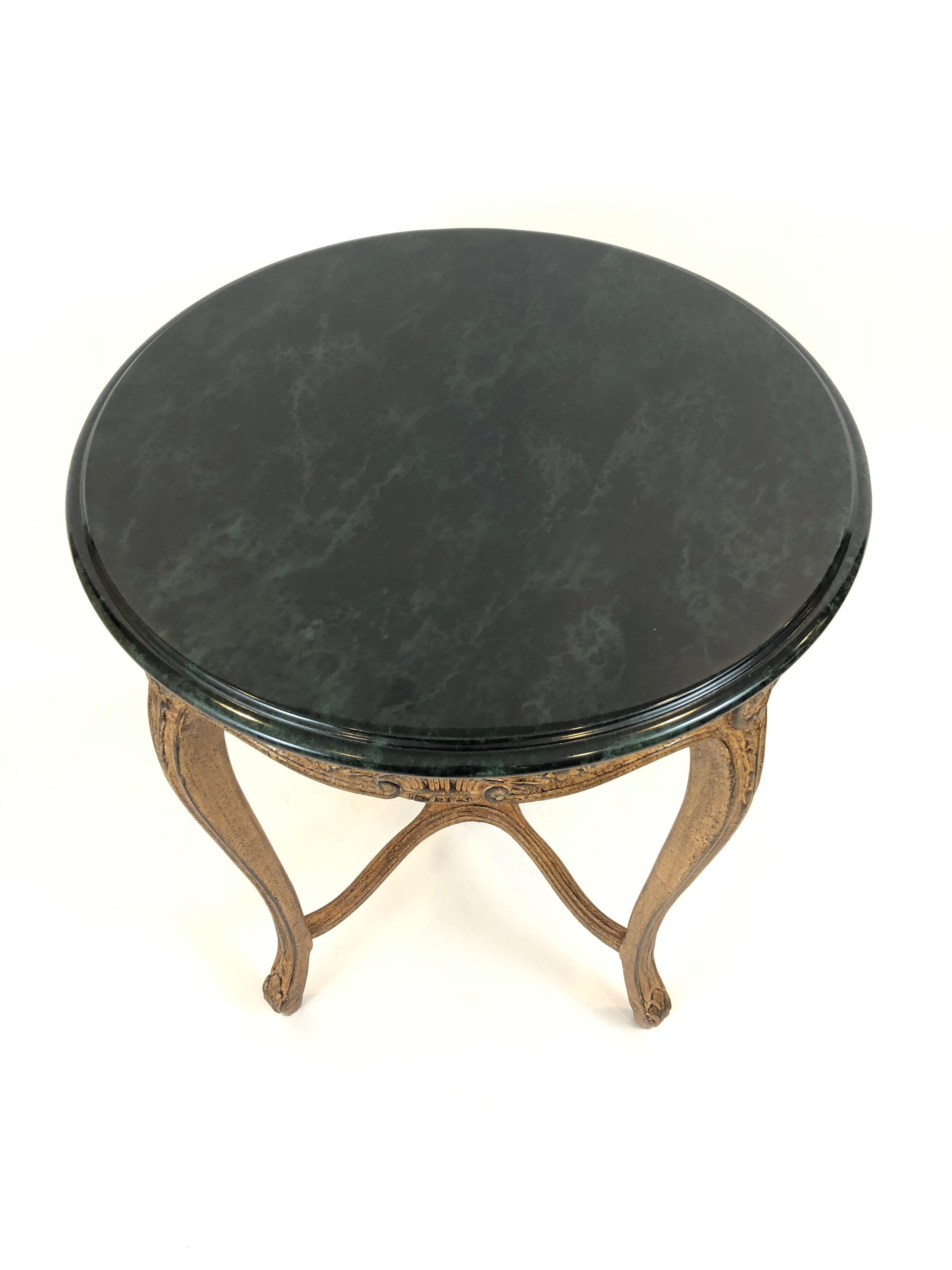 Versatile French style round side table having pretty antiqued gilded faux finished carved wood base and faux green marble top.