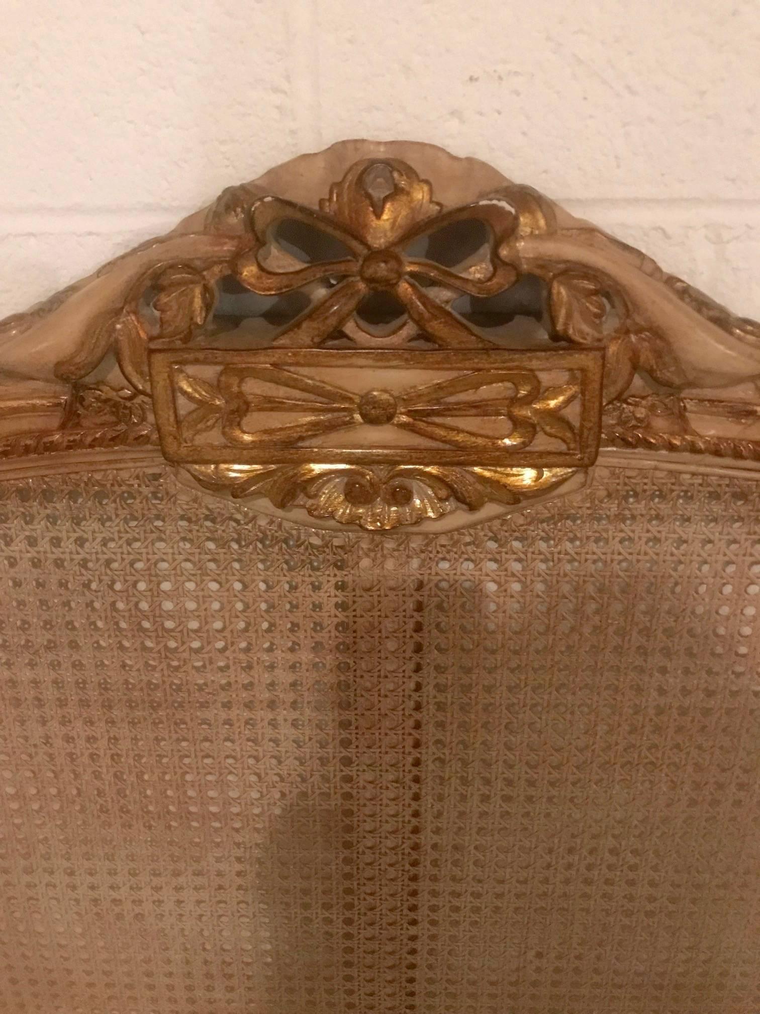 Jolie tête de lit de style français peinte en crème avec des embellissements en feuille d'or:: un nœud en haut et un joli cannage.